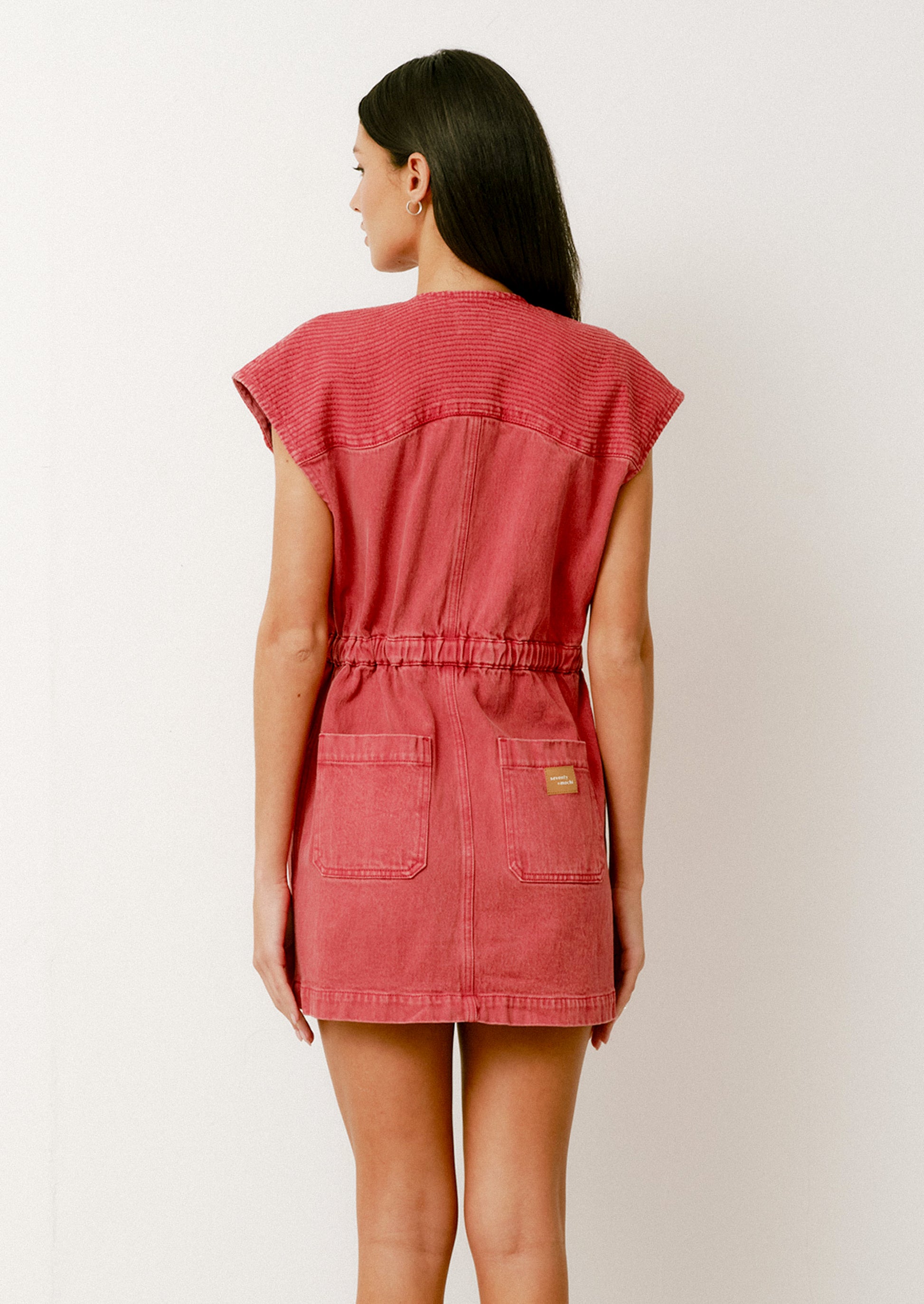 A person wearing a denim mini dress in red with cap sleeves and front pockets.