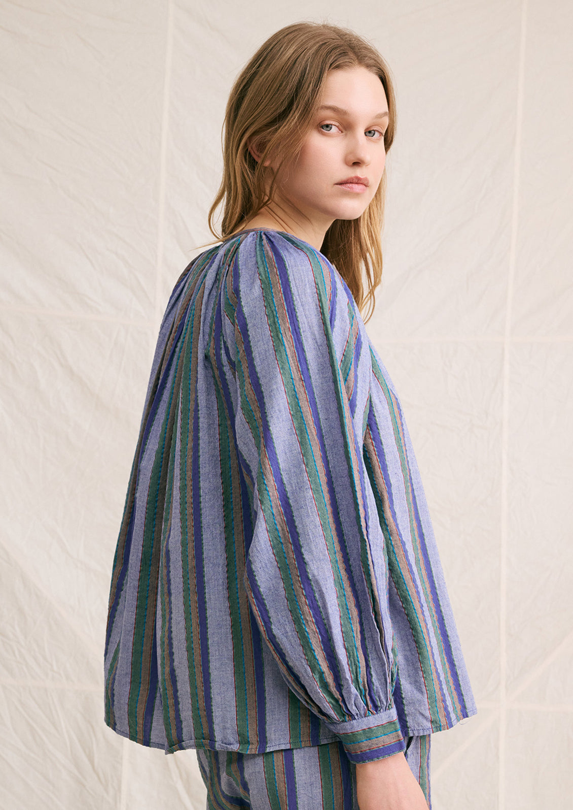 A woman wearing a blue chambray blouse with green and brown stripe pattern.