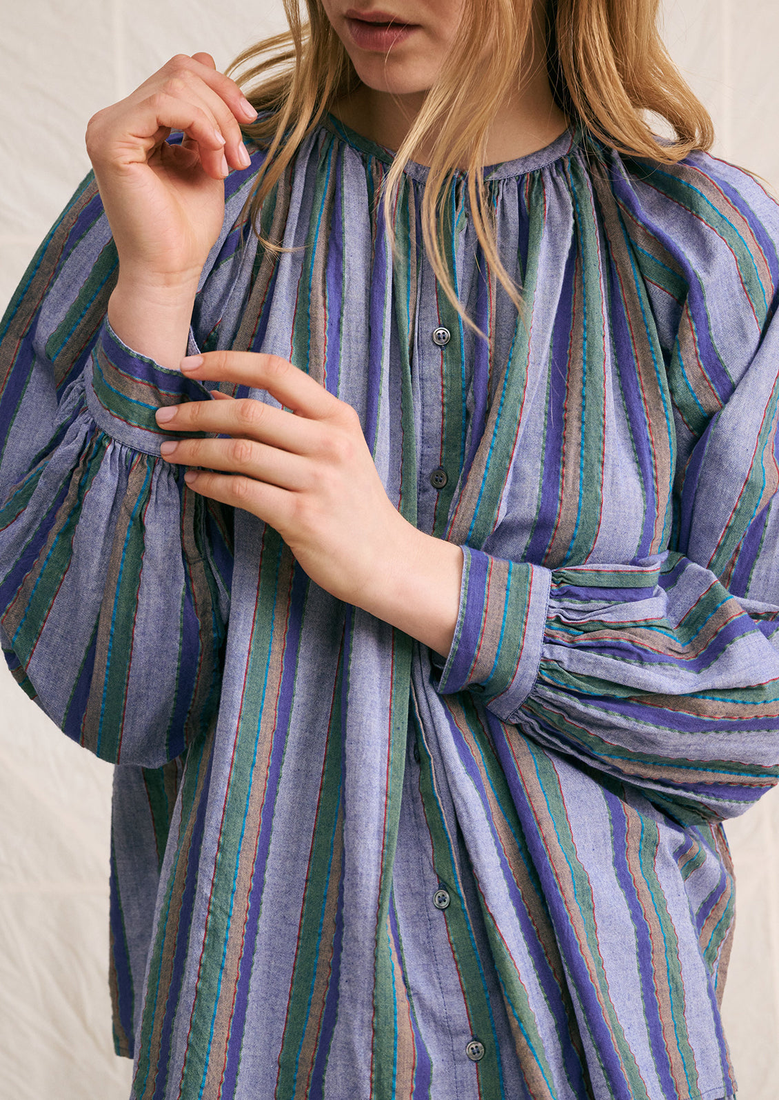 A woman wearing a blue chambray blouse with green and brown stripe pattern.