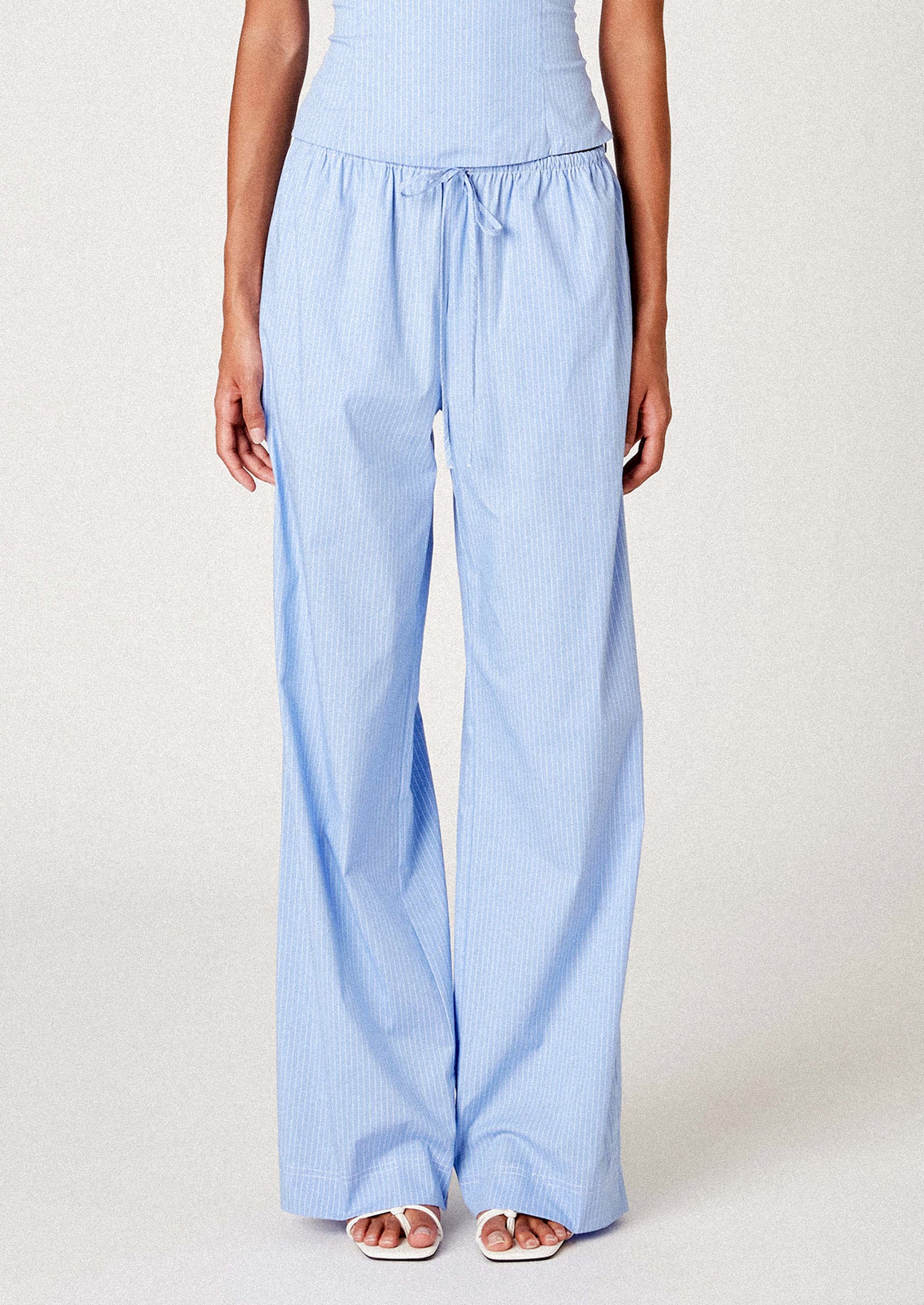 A person wearing a pair of pajama-inspired pants in blue with white pinstripe.