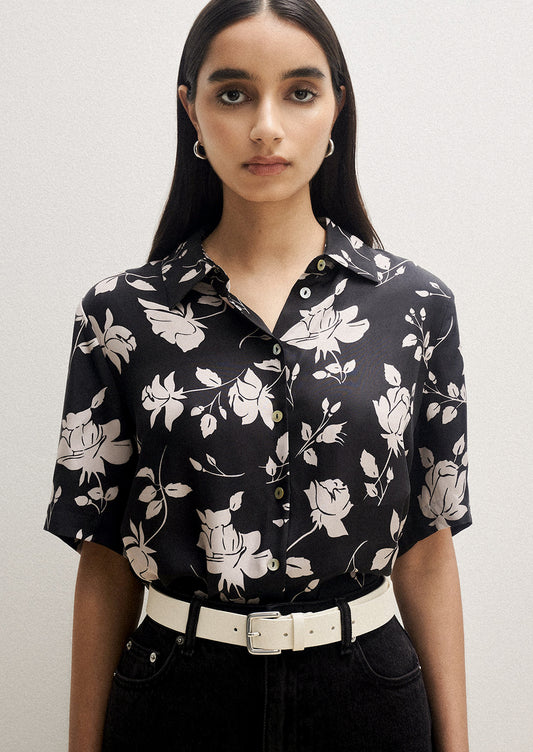 A person wearing a short sleeve collared shirt in black with white floral pattern.