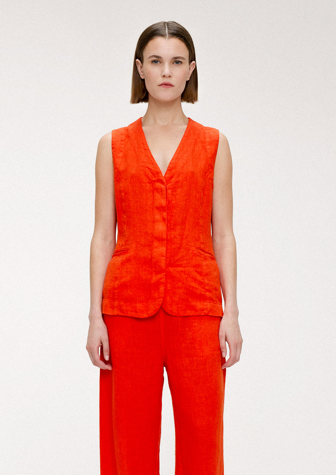 A woman wearing a sleeveless v-neck linen top in red orange hue.