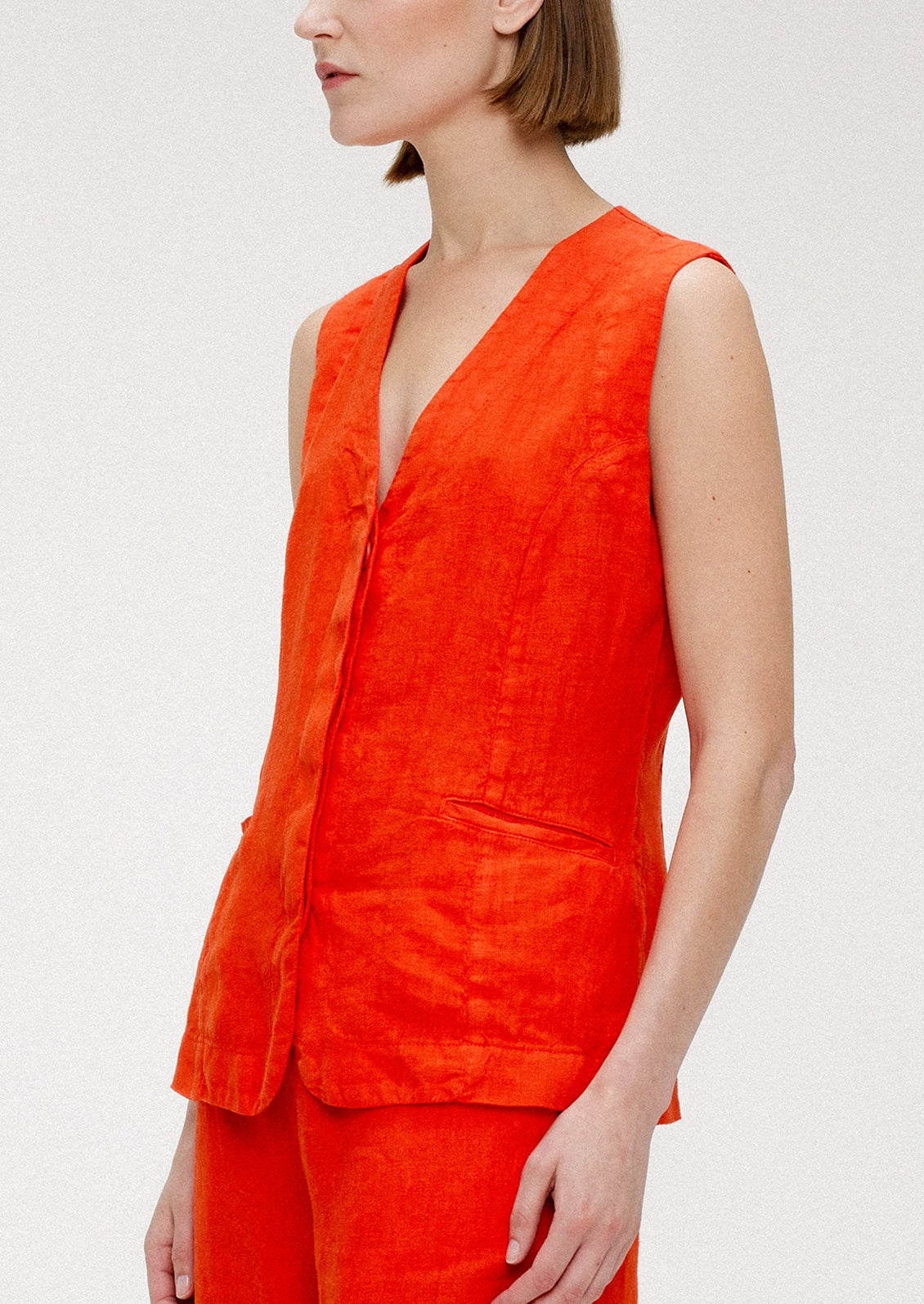 A woman wearing a sleeveless v-neck linen top in red orange hue.