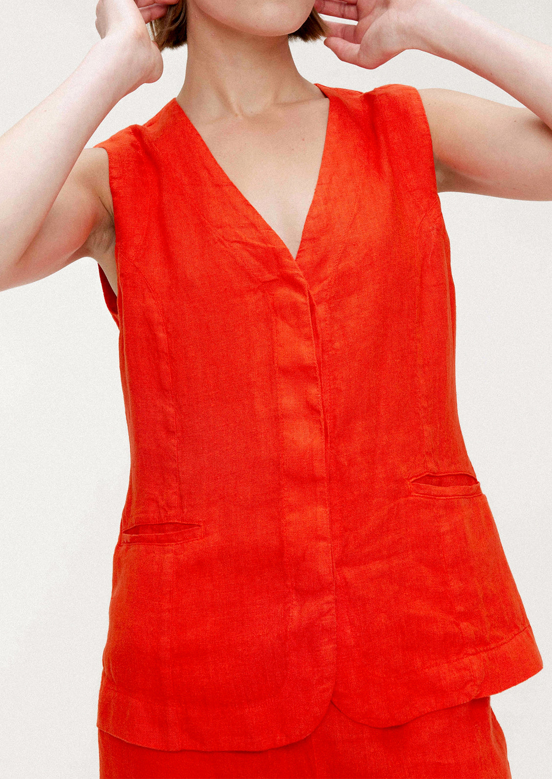 A woman wearing a sleeveless v-neck linen top in red orange hue.