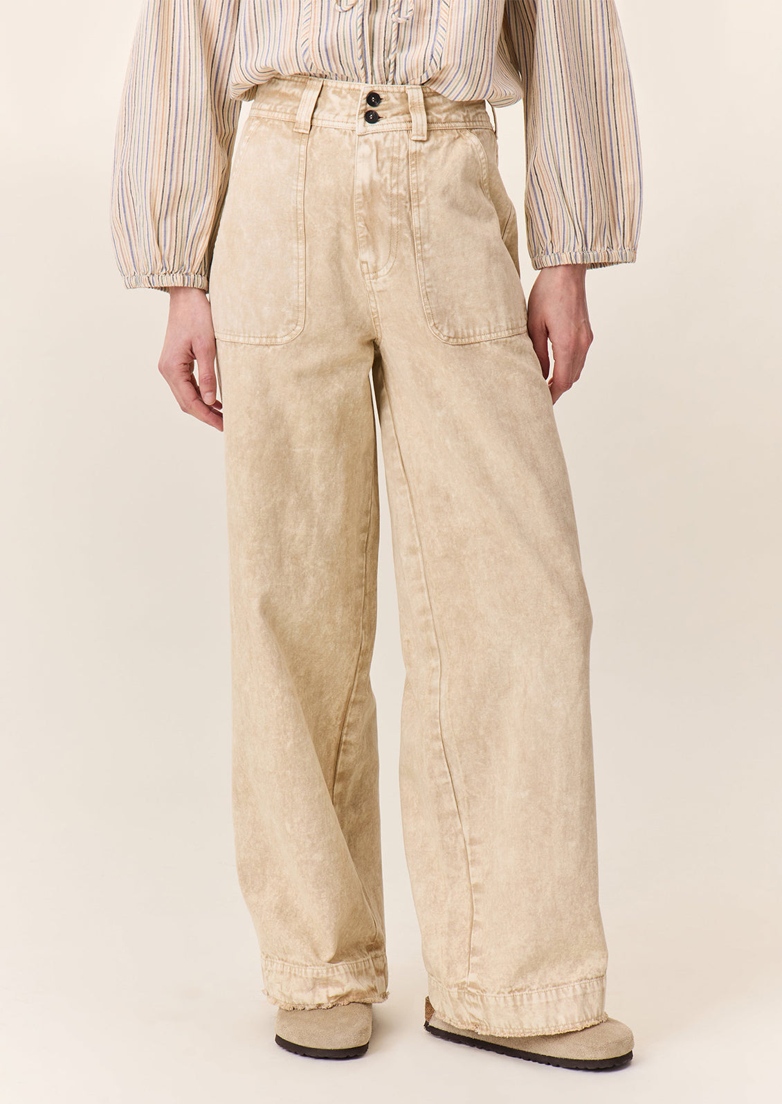 A person wearing a pair of wide leg pants in sand stonewash fabric.