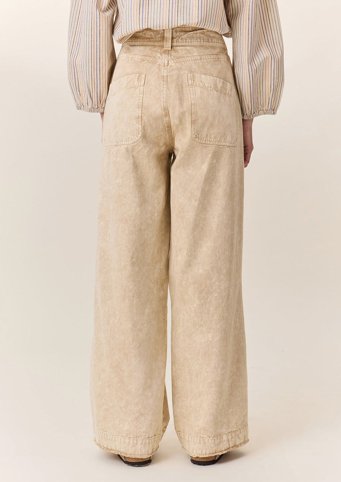 A person wearing a pair of wide leg pants in sand stonewash fabric.