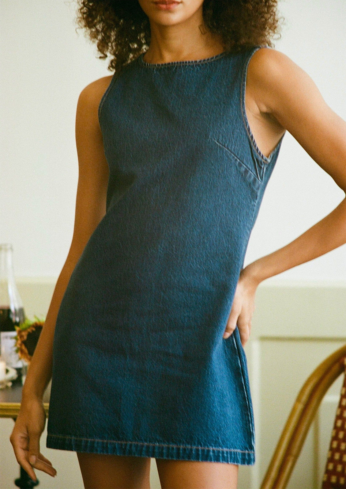 A woman wearing a short shift dress in dark blue denim.