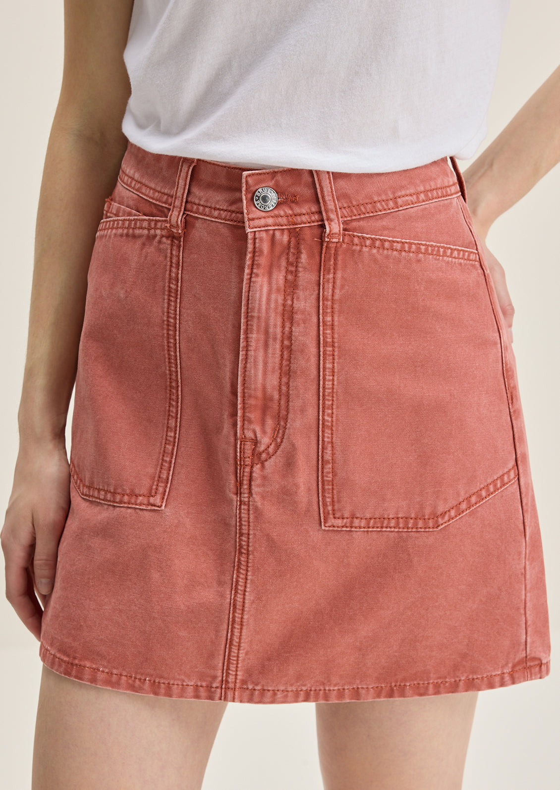 A person wearing a mini skirt in coral colored denim.