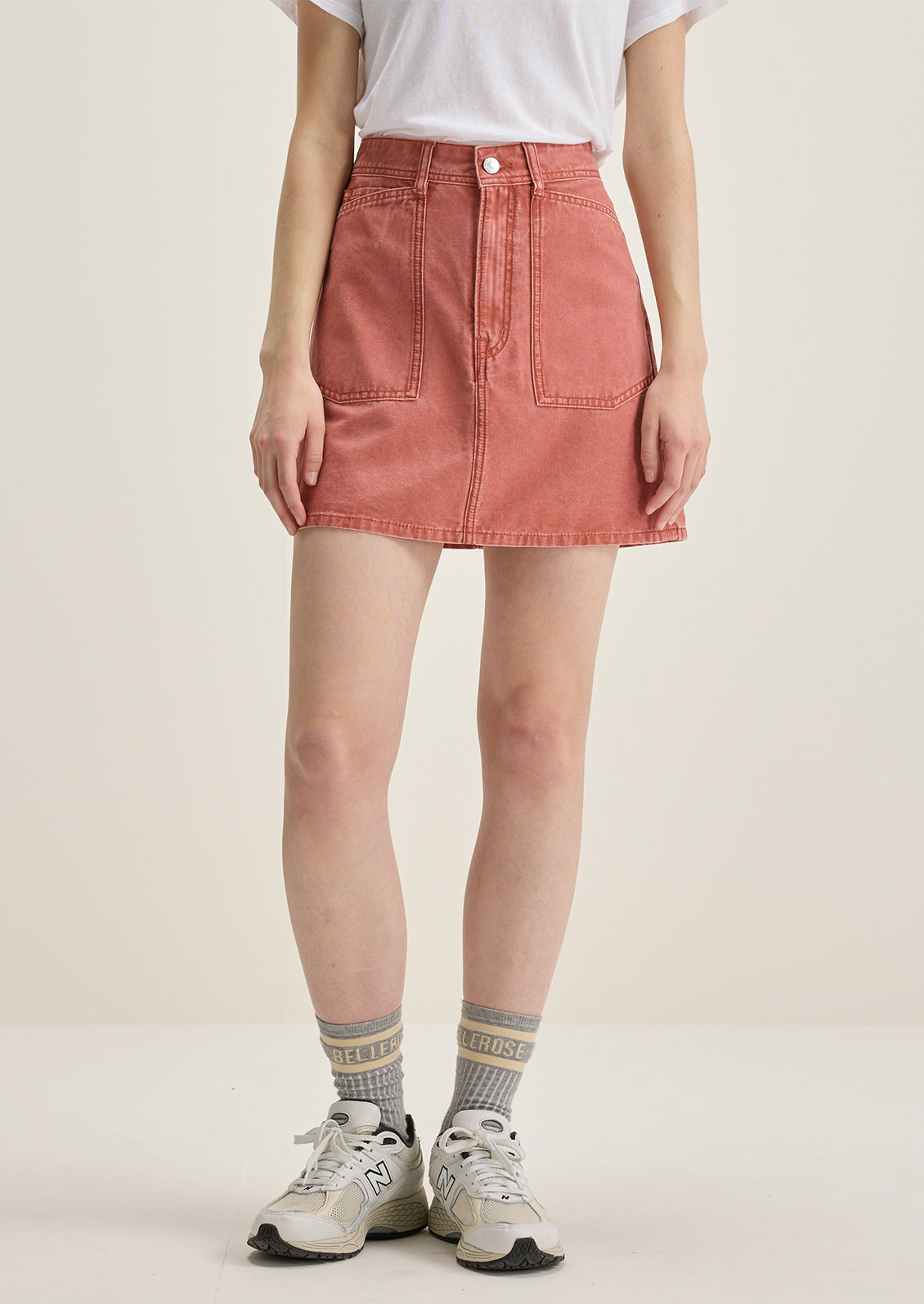 A person wearing a mini skirt in coral colored denim.