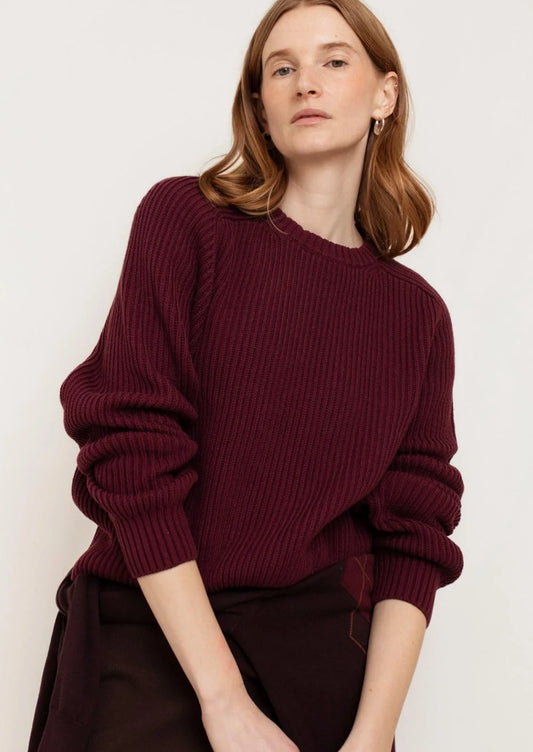 A person wearing a chunky rib knit sweater in burgundy.