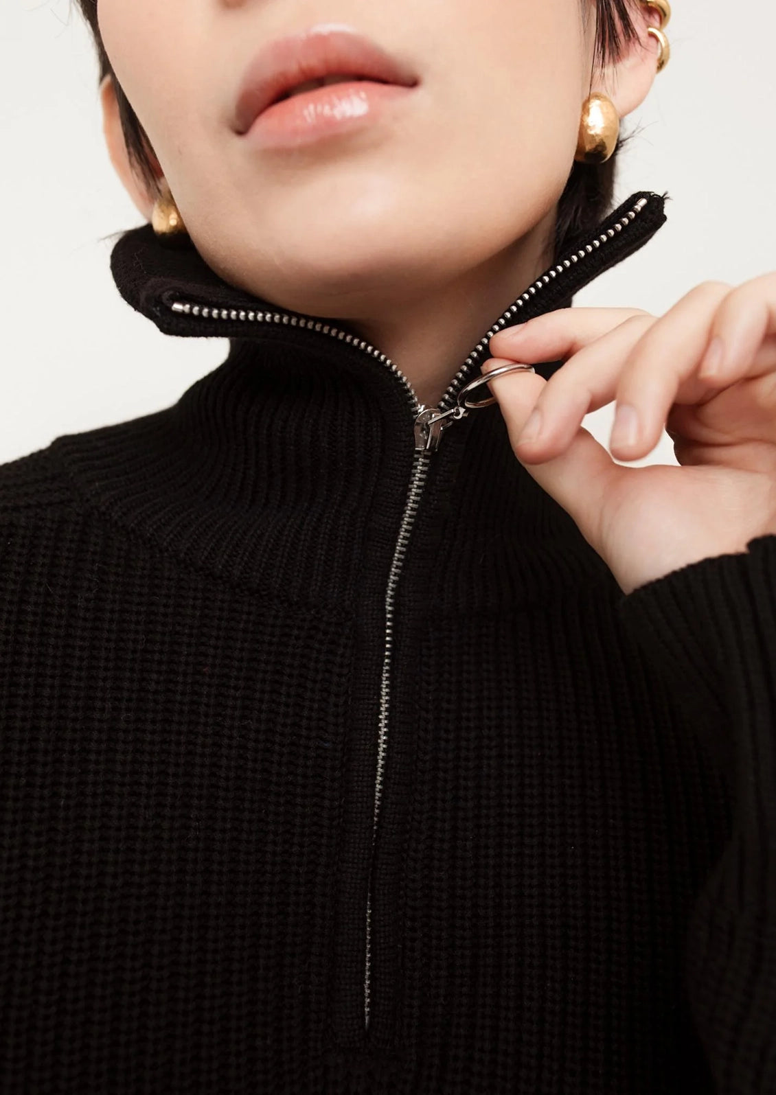 A person wearing a black sweater with silver zip at funnel neck.