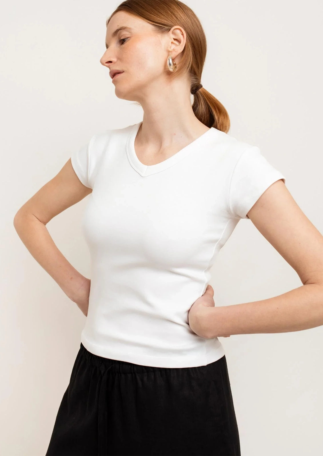 Woman wearing a white t-shirt and black pants against a plain background