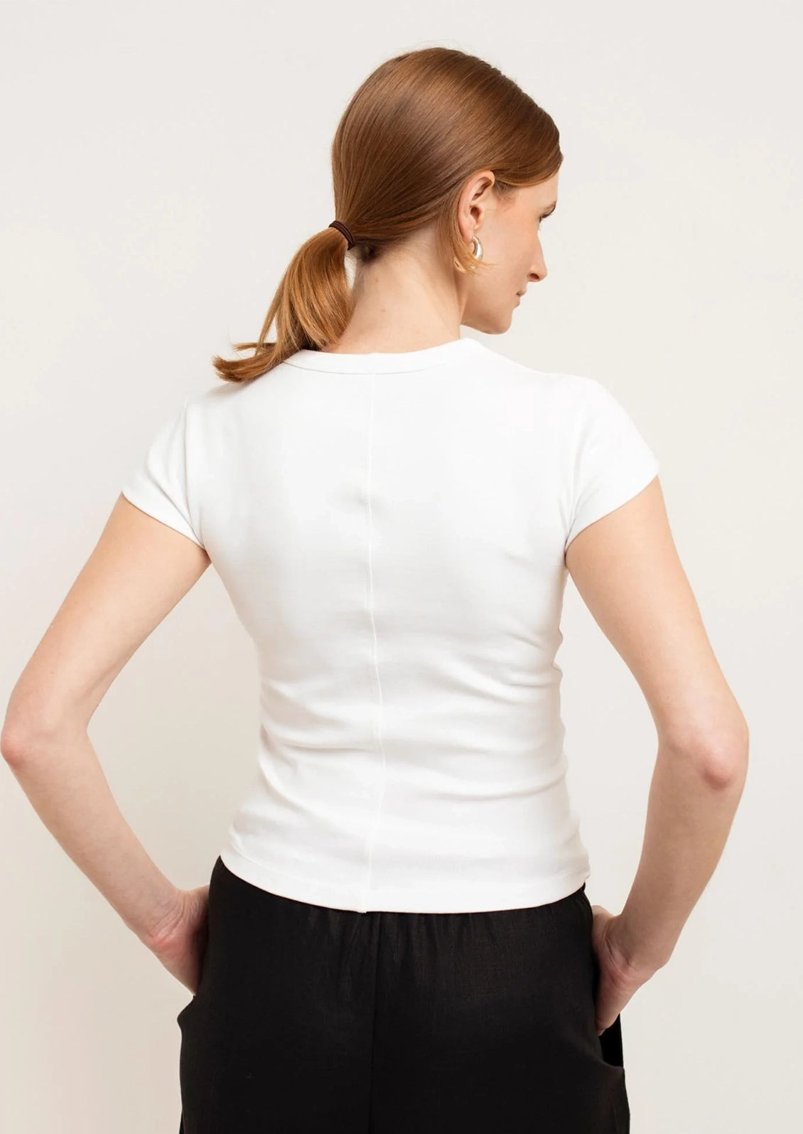 Woman wearing a white t-shirt and black pants against a plain background