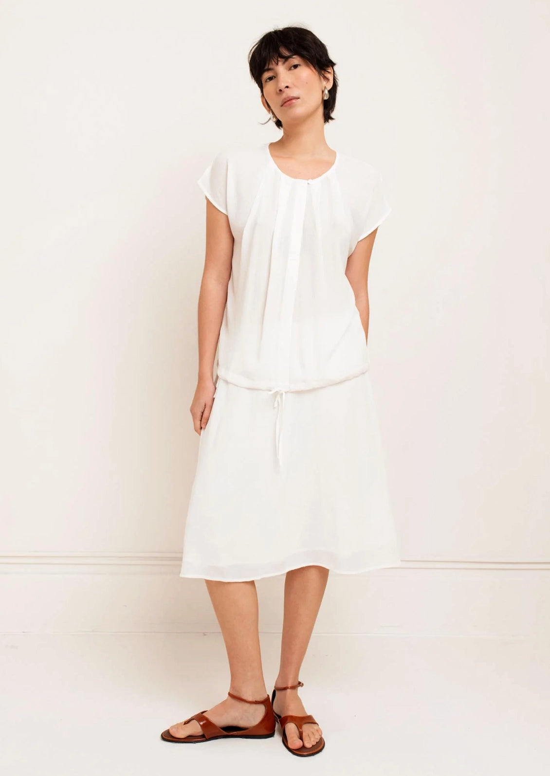 Woman wearing a white outfit with brown sandals against a plain background