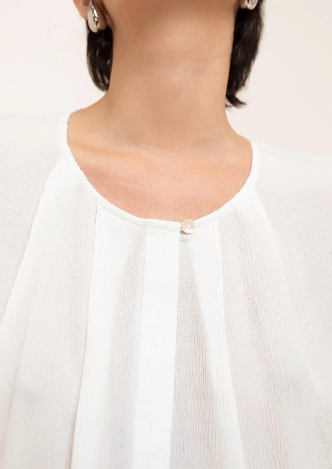 Close-up of a person wearing a white blouse with a plain background