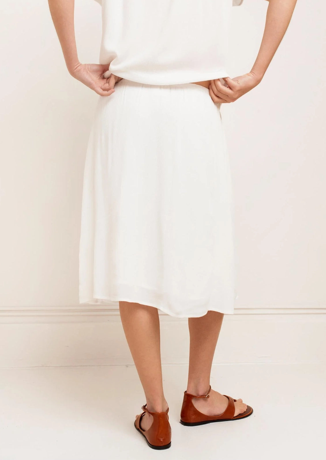 Person wearing a white dress with brown sandals on a plain background