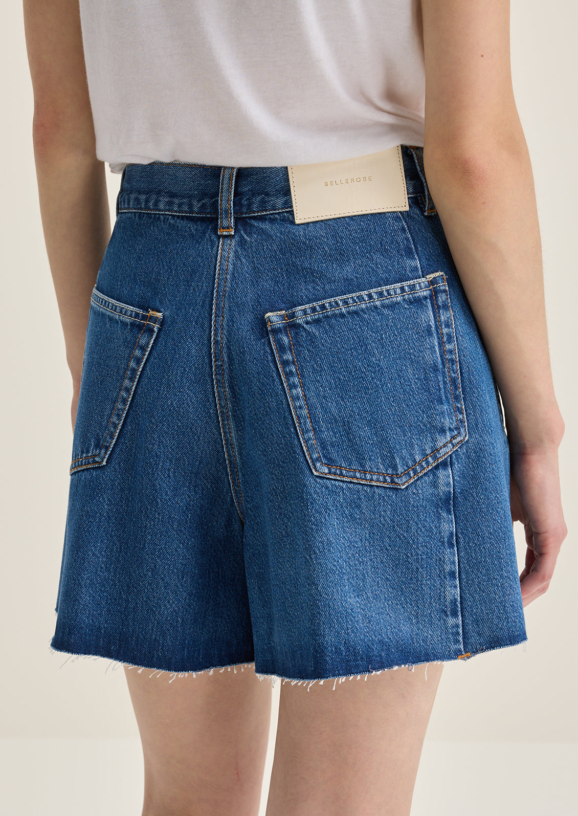 A person wearing a pair of pleated denim shorts in true medium blue wash.