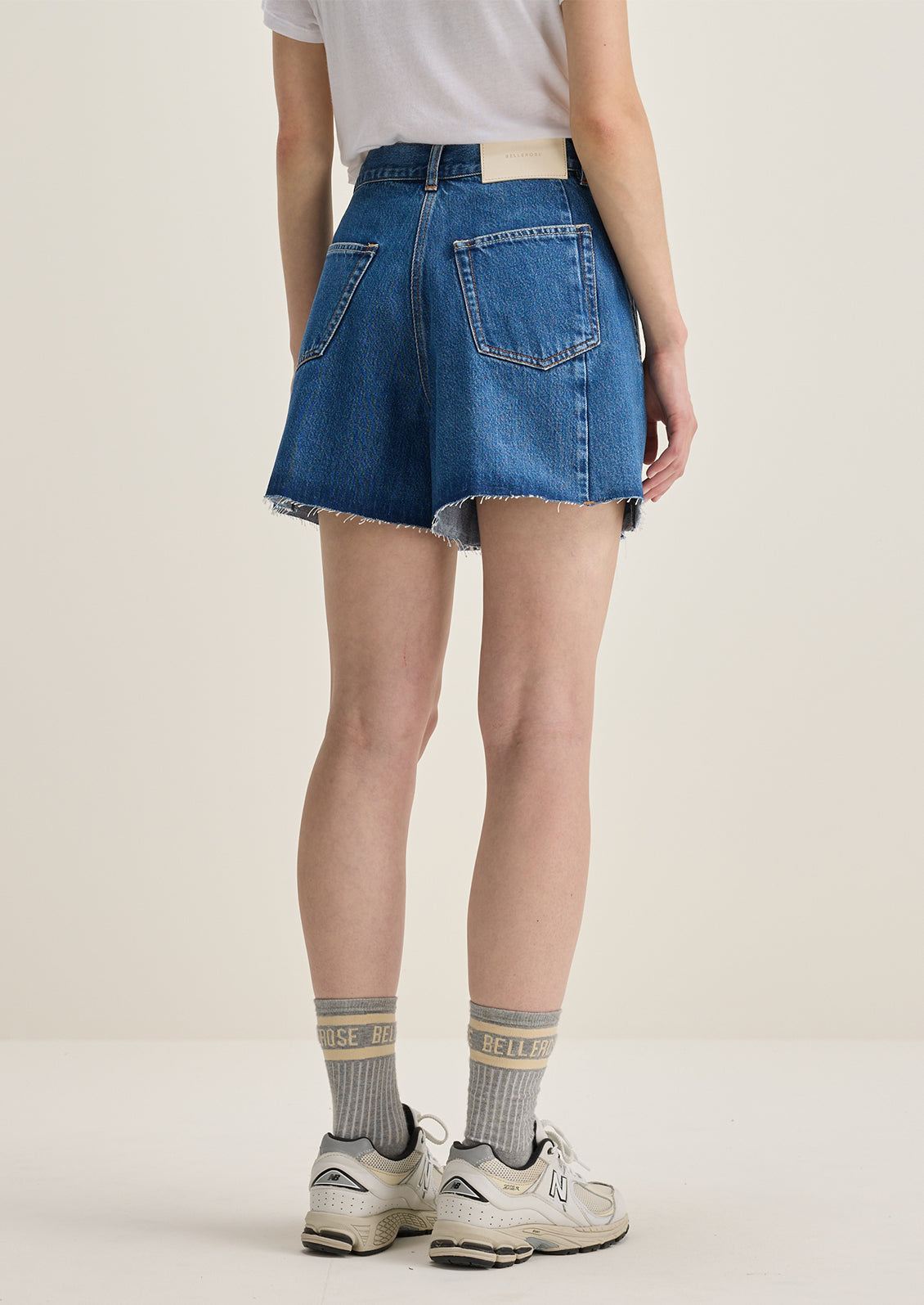 A person wearing a pair of pleated denim shorts in true medium blue wash.
