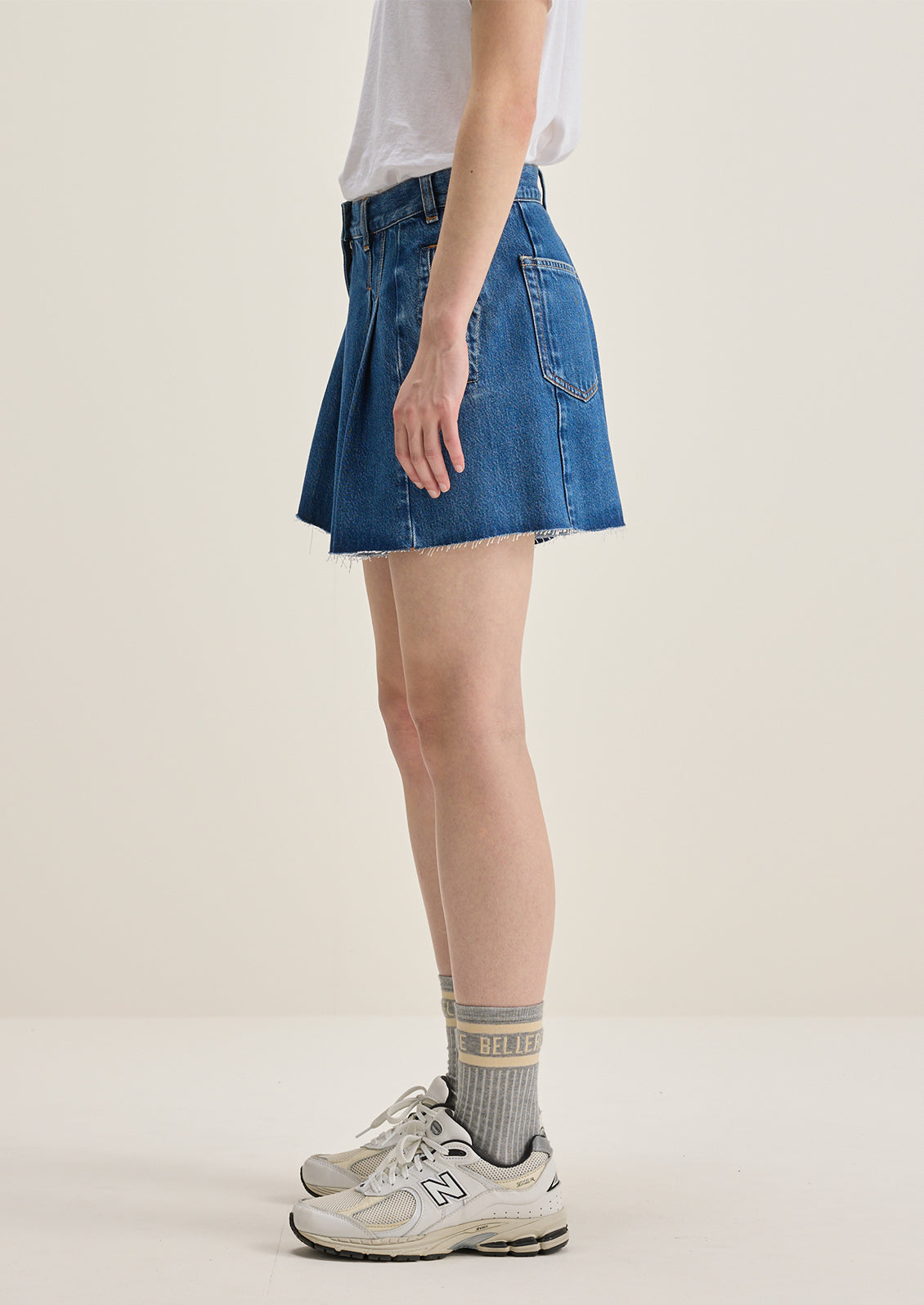 A person wearing a pair of pleated denim shorts in true medium blue wash.