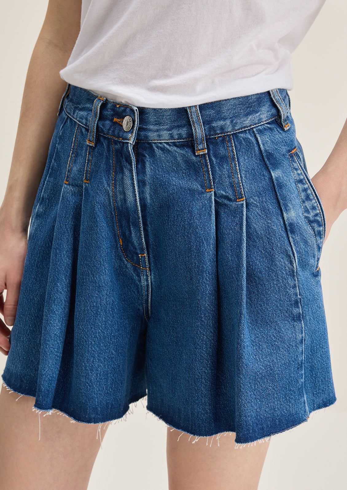A person wearing a pair of pleated denim shorts in true medium blue wash.
