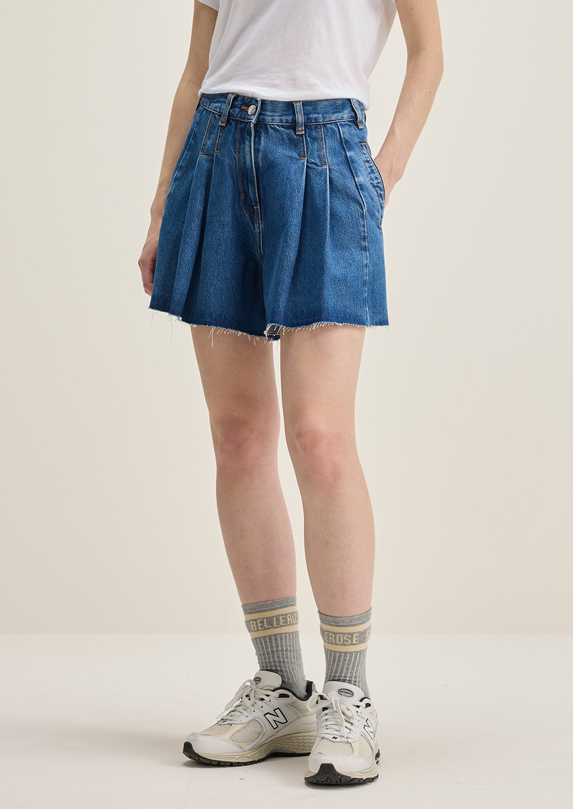 A person wearing a pair of pleated denim shorts in true medium blue wash.