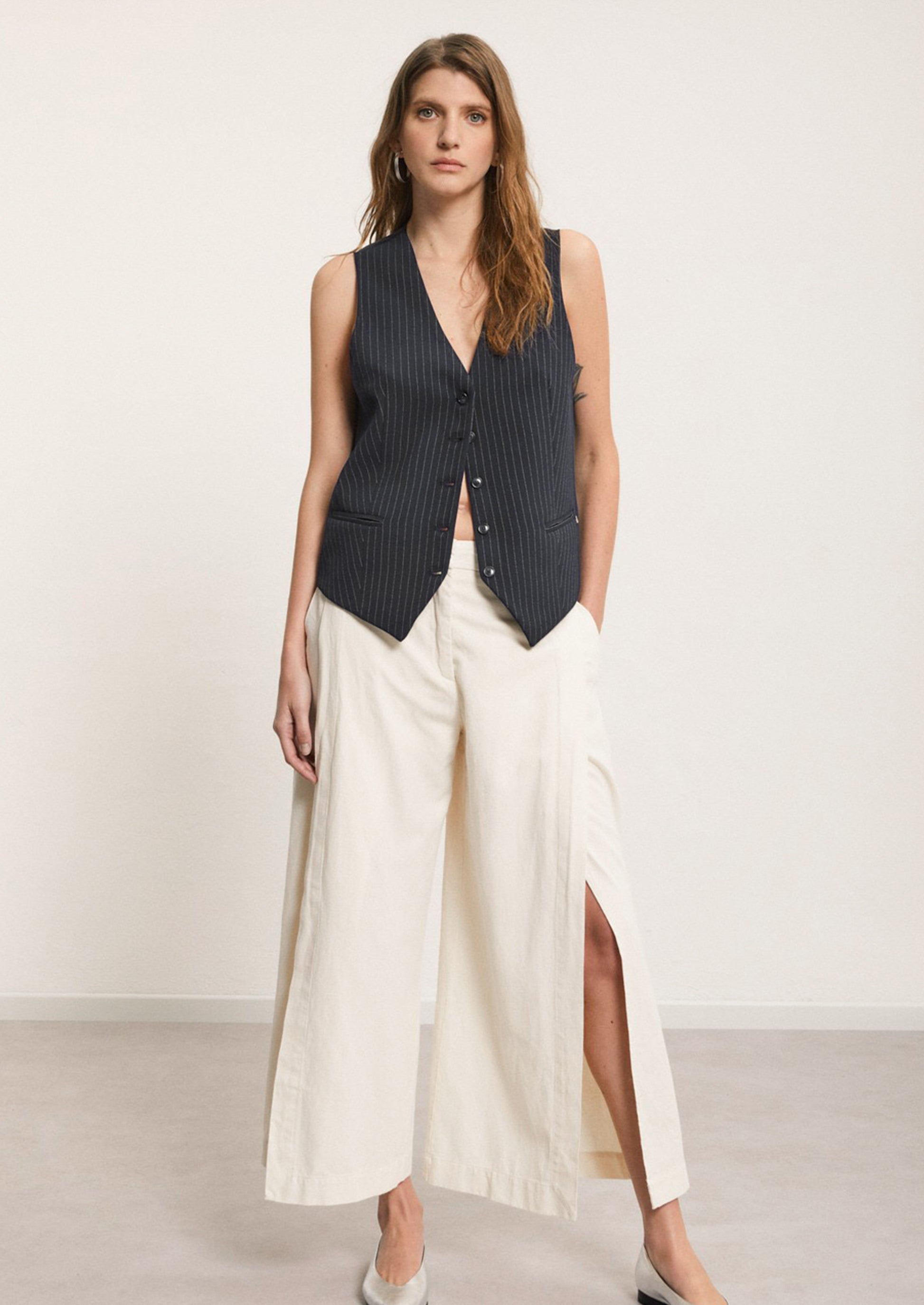 A woman wearing a pair of ankle length cream pants with split leg.