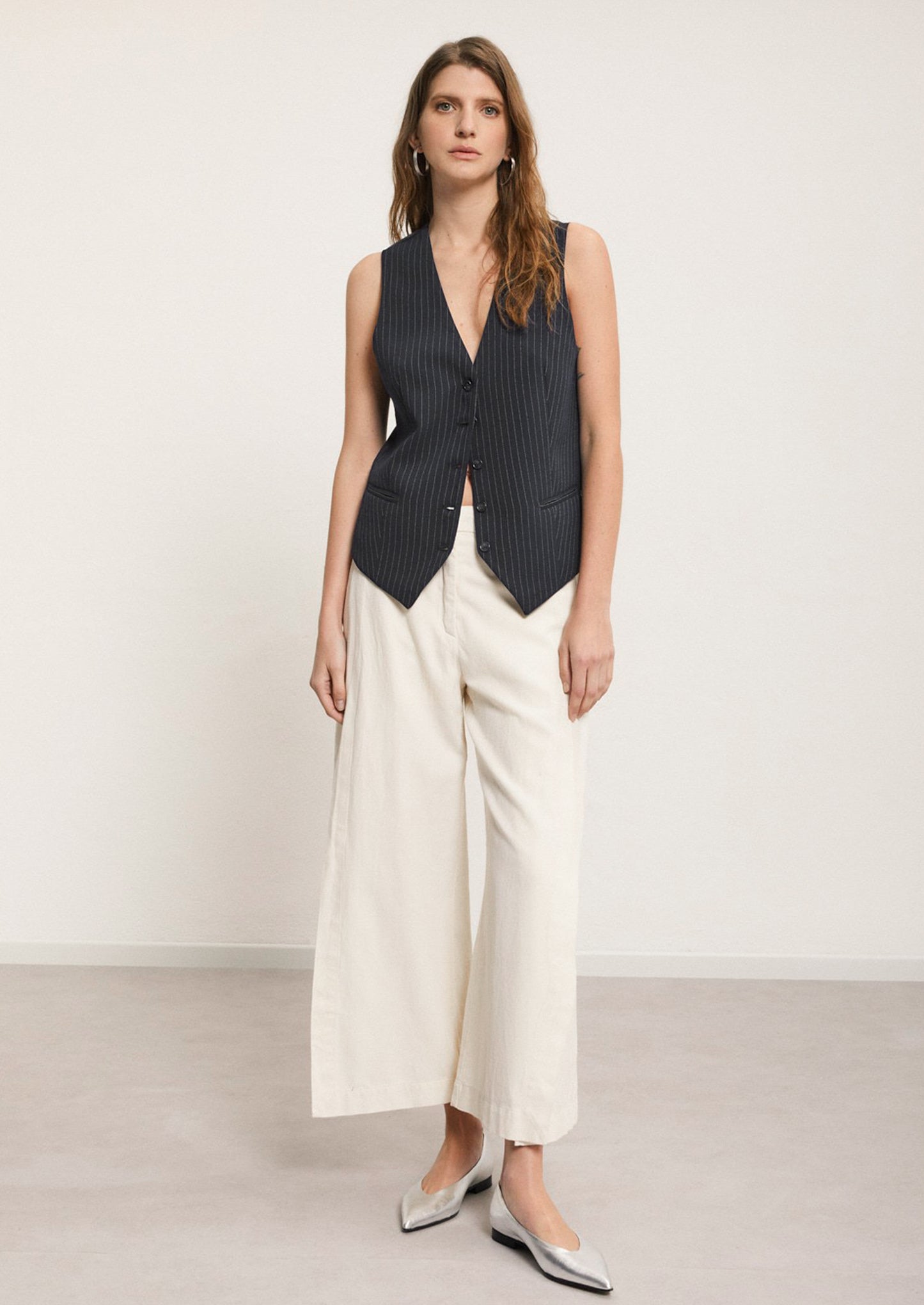 A woman wearing a pair of ankle length cream pants with split leg.