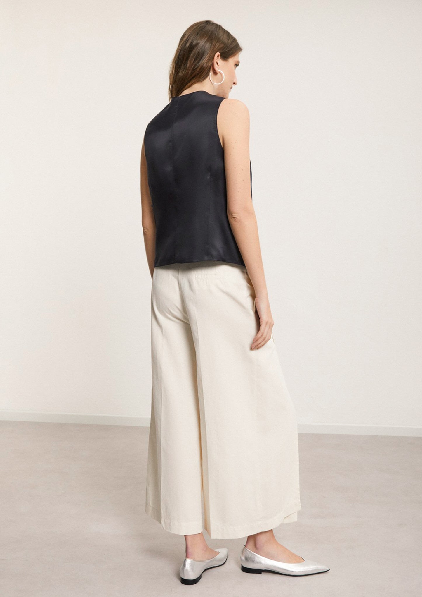 A woman wearing a pair of ankle length cream pants with split leg.