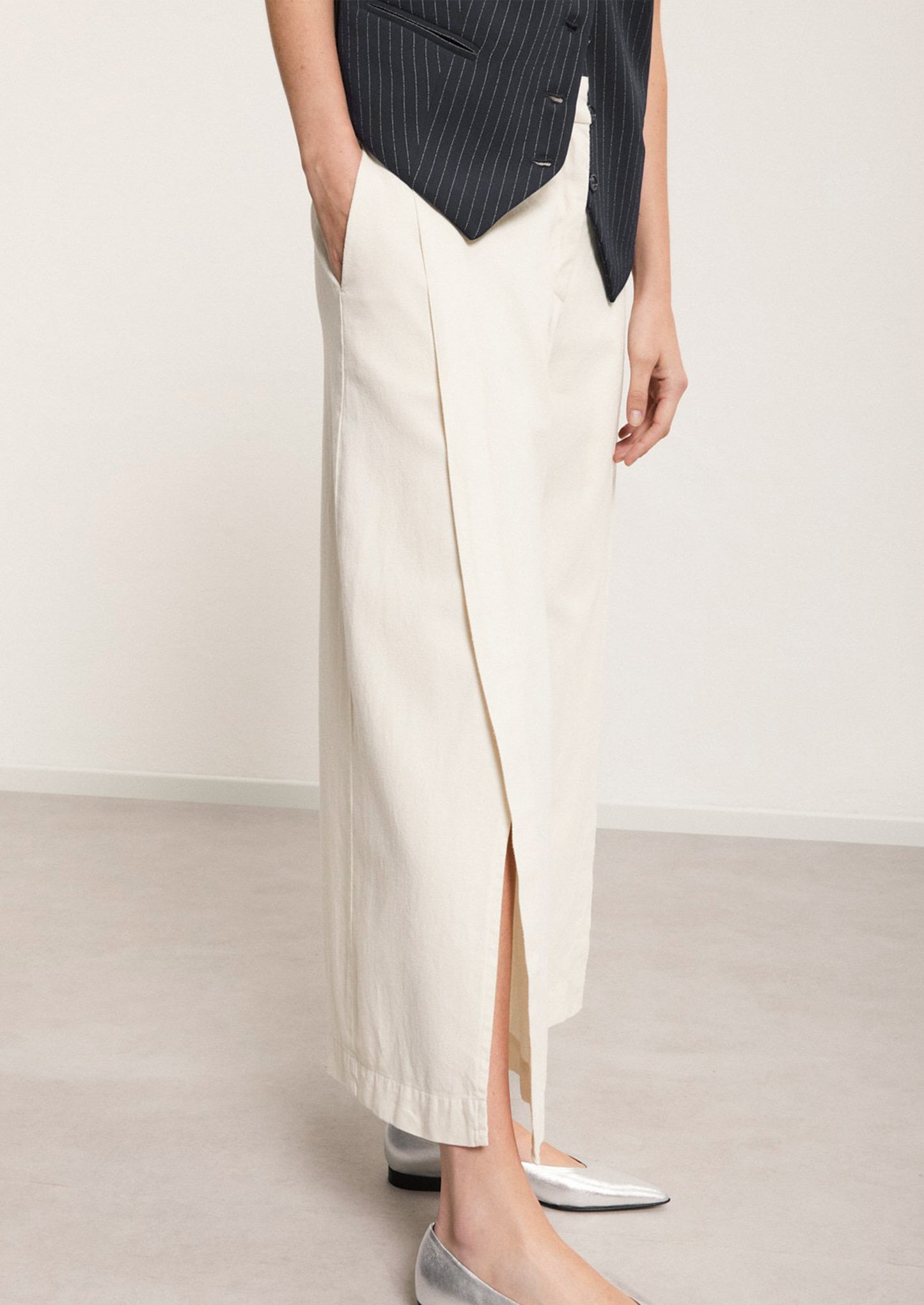 A woman wearing a pair of ankle length cream pants with split leg.