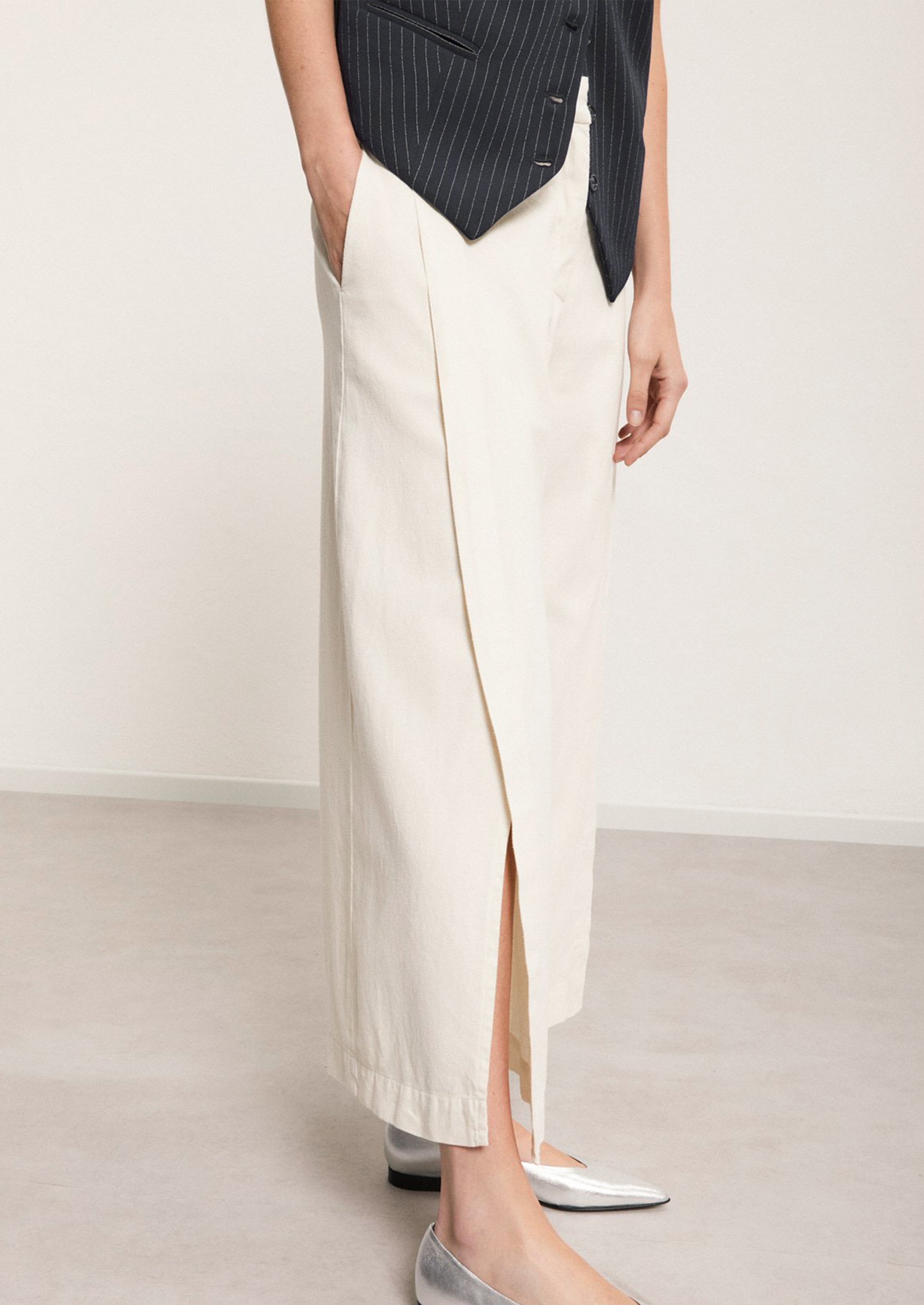 A woman wearing a pair of ankle length cream pants with split leg.