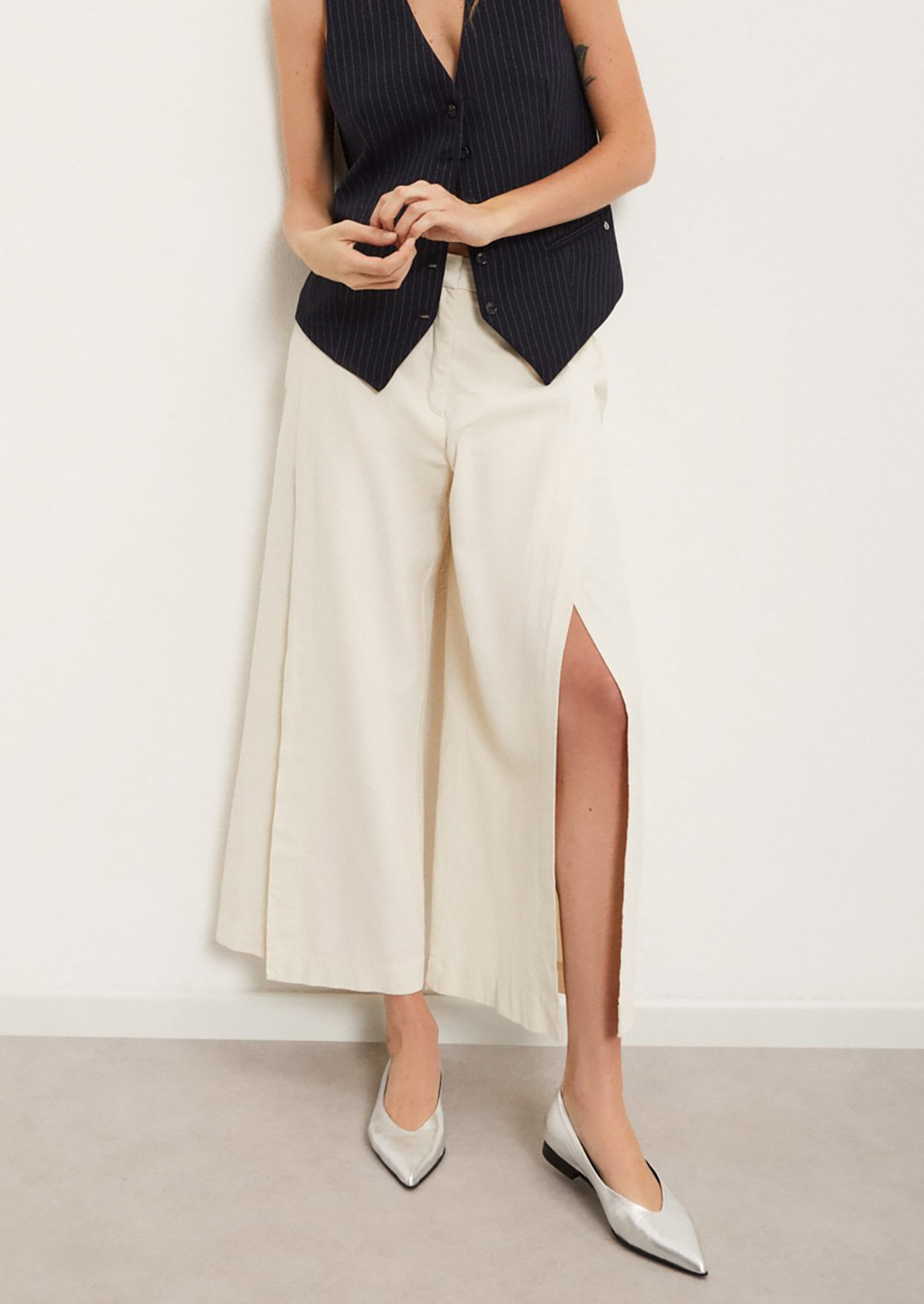 A woman wearing a pair of ankle length cream pants with split leg.