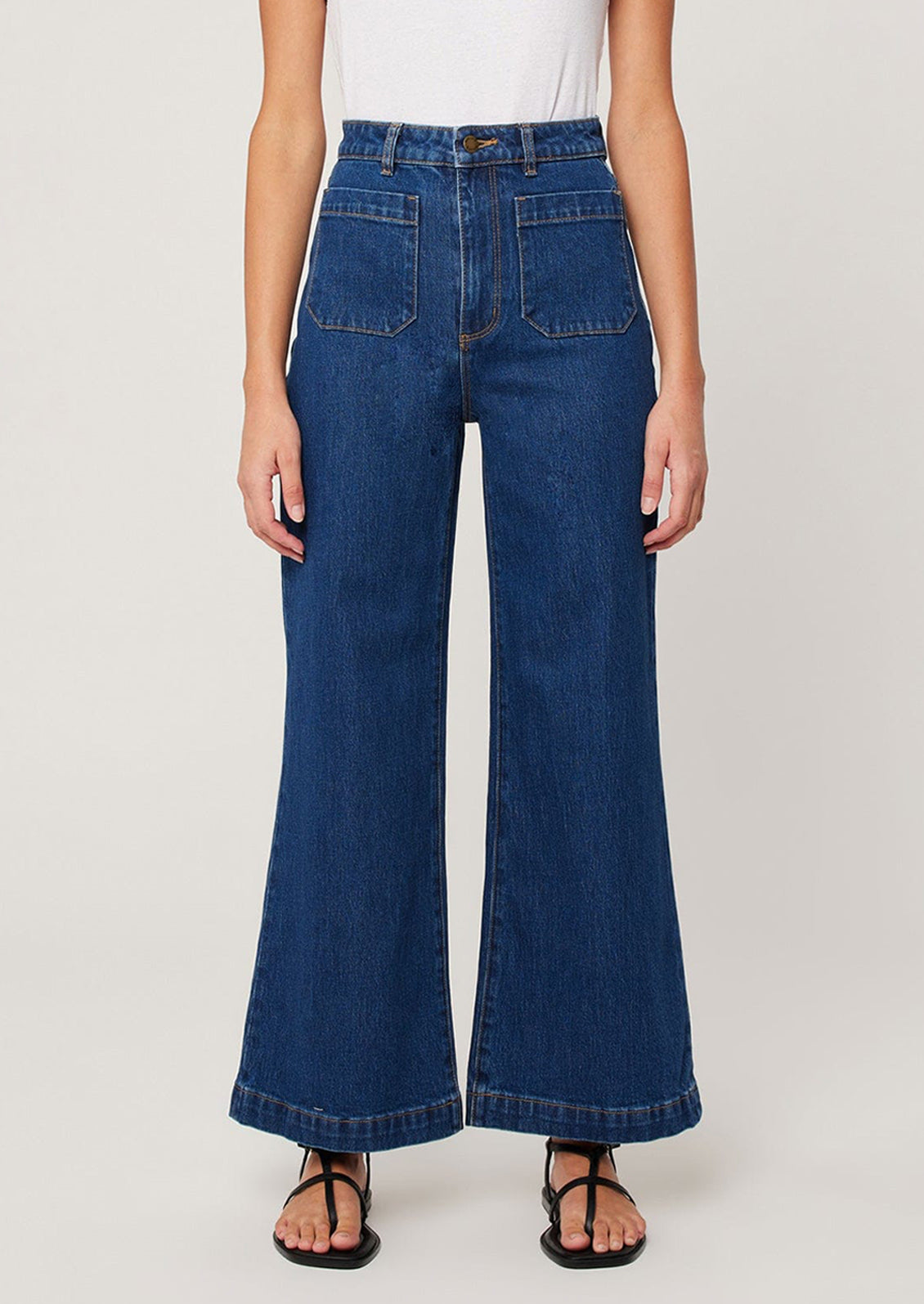 A woman wearing a pair of dark wash jeans with patch pockets at hips and wide leg shape.