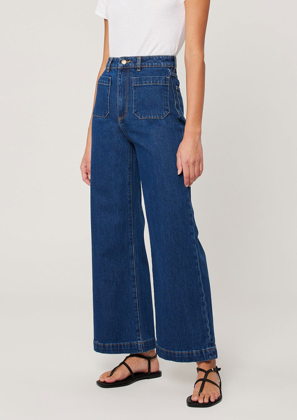 A woman wearing a pair of dark wash jeans with patch pockets at hips and wide leg shape.