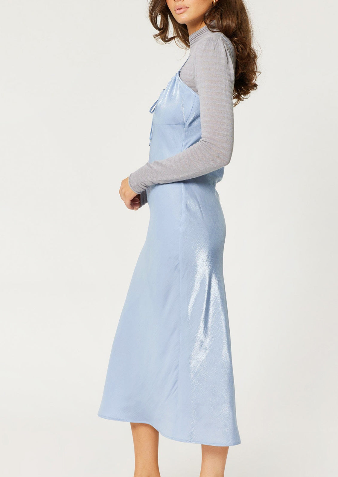 A woman wearing a periwinkle color sleeveless satin dress with empire silhouette.