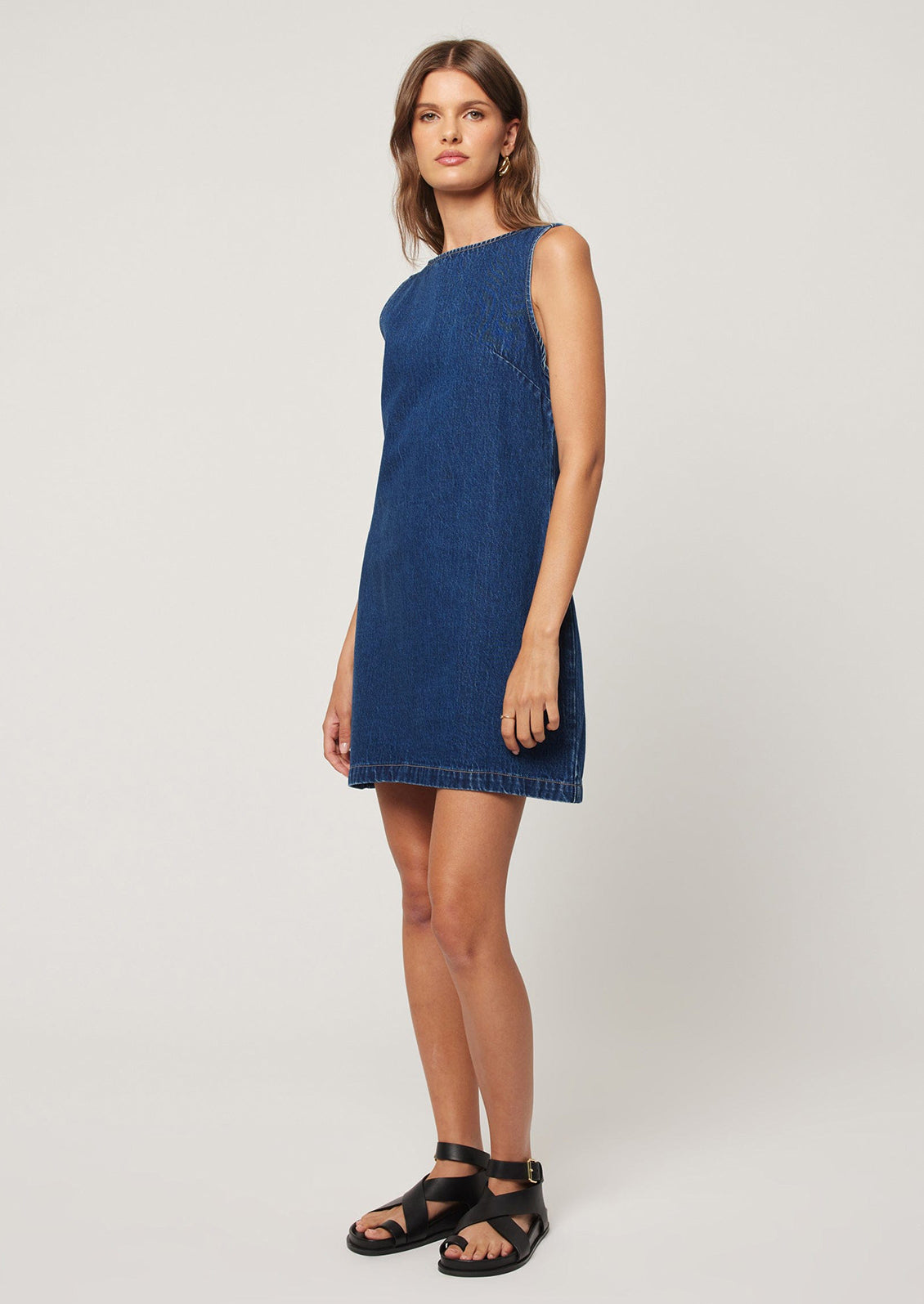 A woman wearing a short shift dress in dark blue denim.