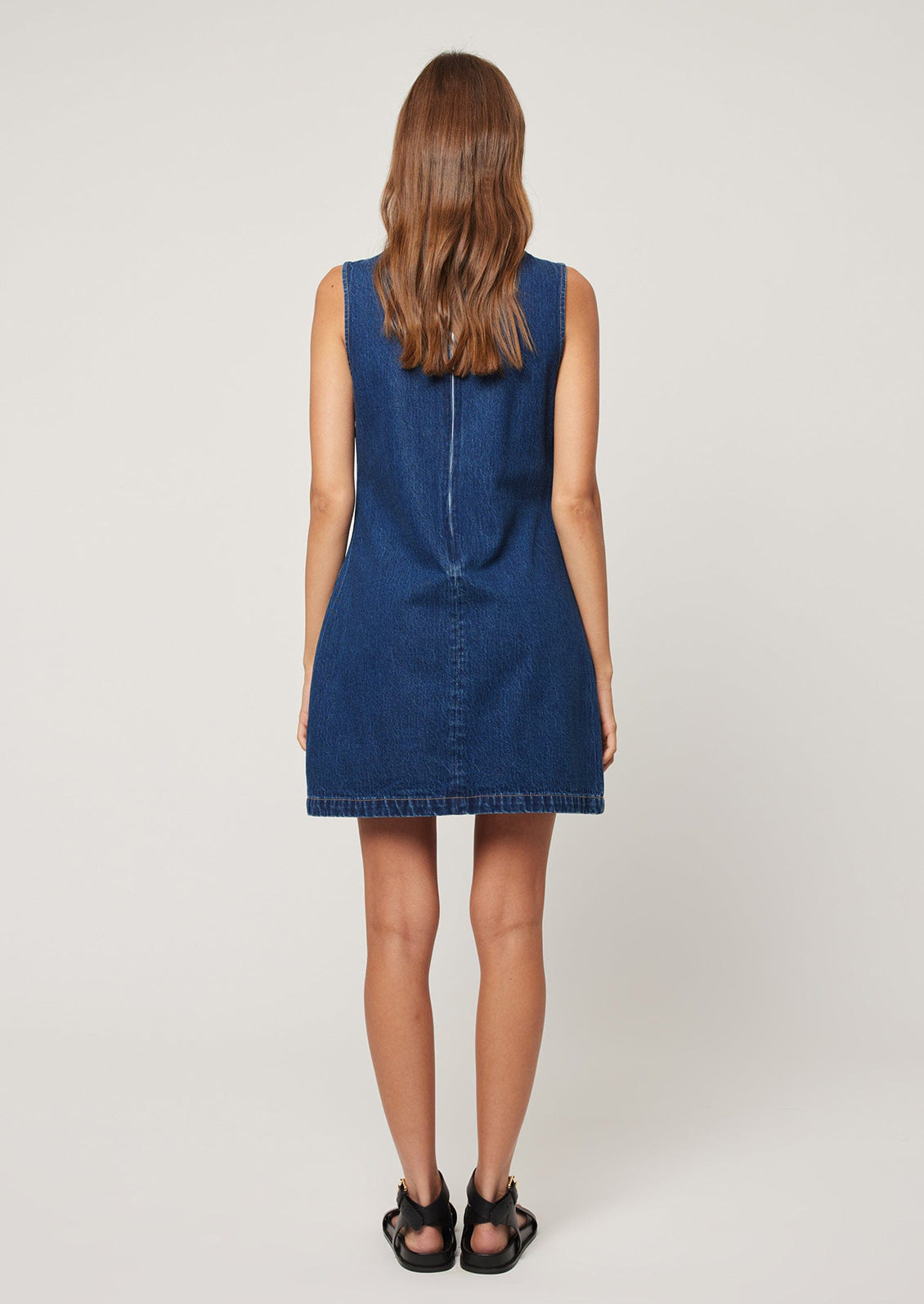 A woman wearing a short shift dress in dark blue denim.