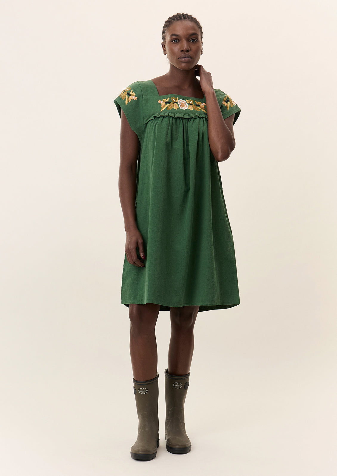 A person wearing a short green dress with yellow floral embroidery.