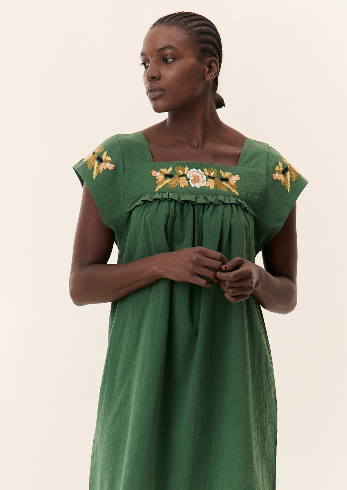 A person wearing a short green dress with yellow floral embroidery.