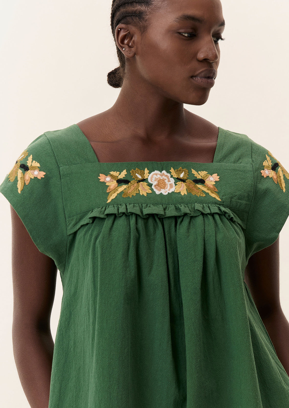 A person wearing a short green dress with yellow floral embroidery.