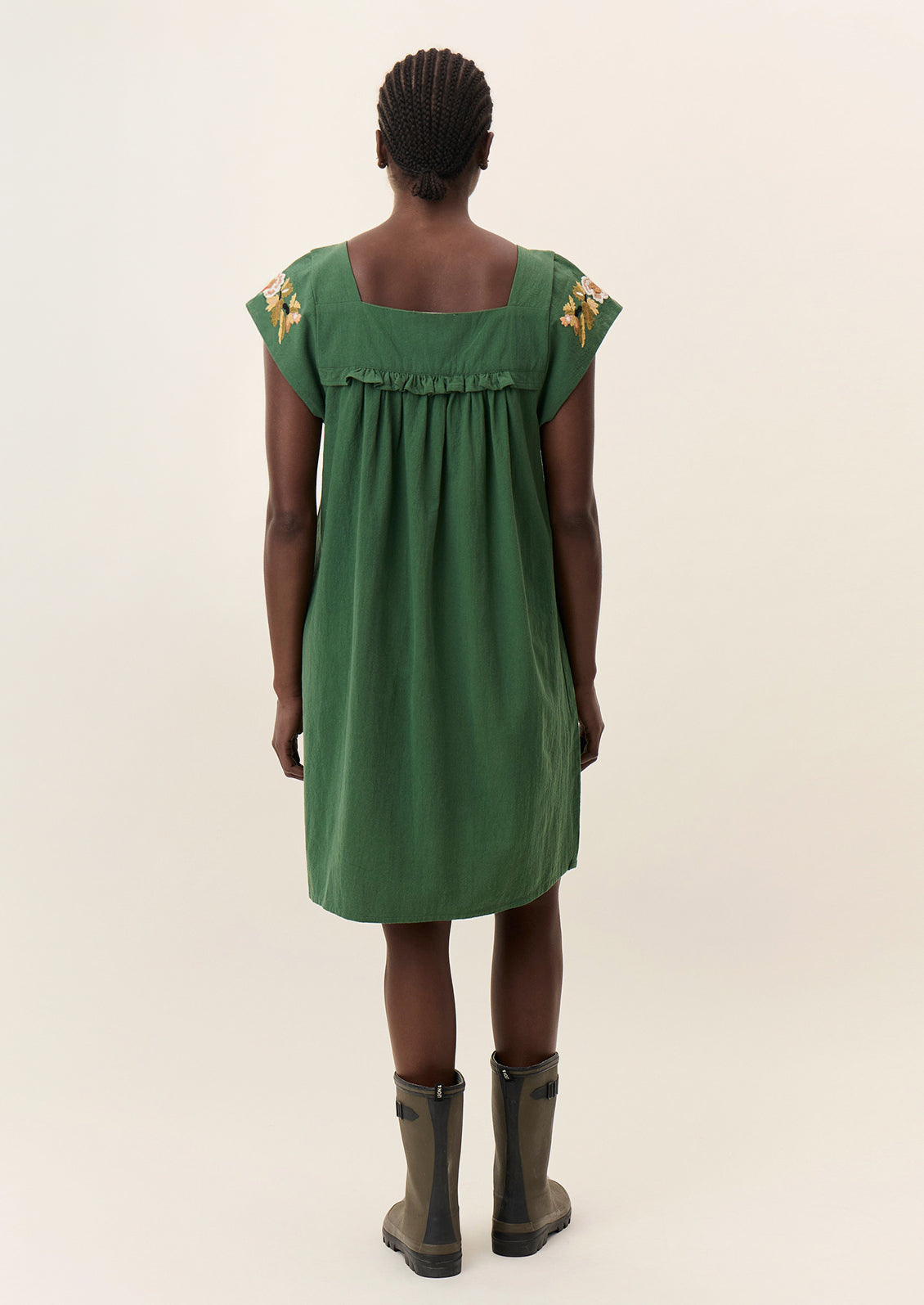 A person wearing a short green dress with yellow floral embroidery.