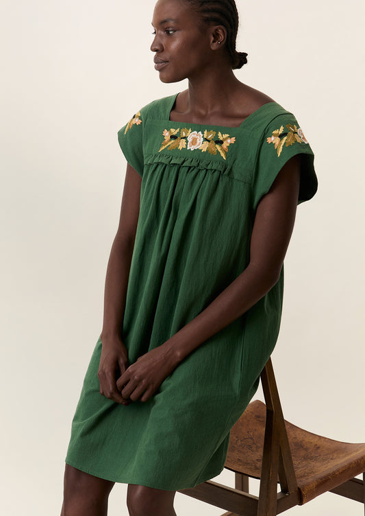A person wearing a short green dress with yellow floral embroidery.