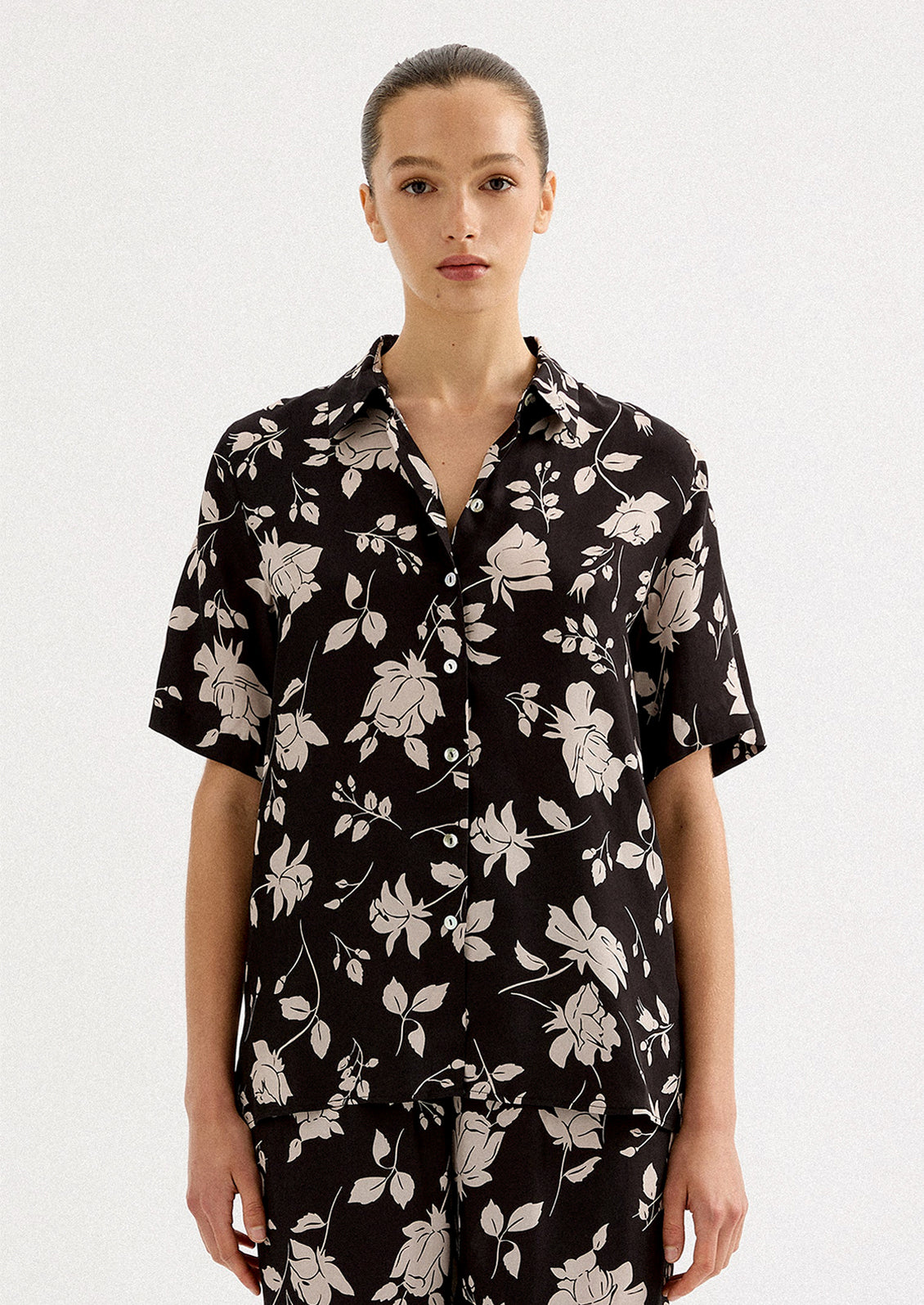 A person wearing a short sleeve collared shirt in black with white floral pattern.