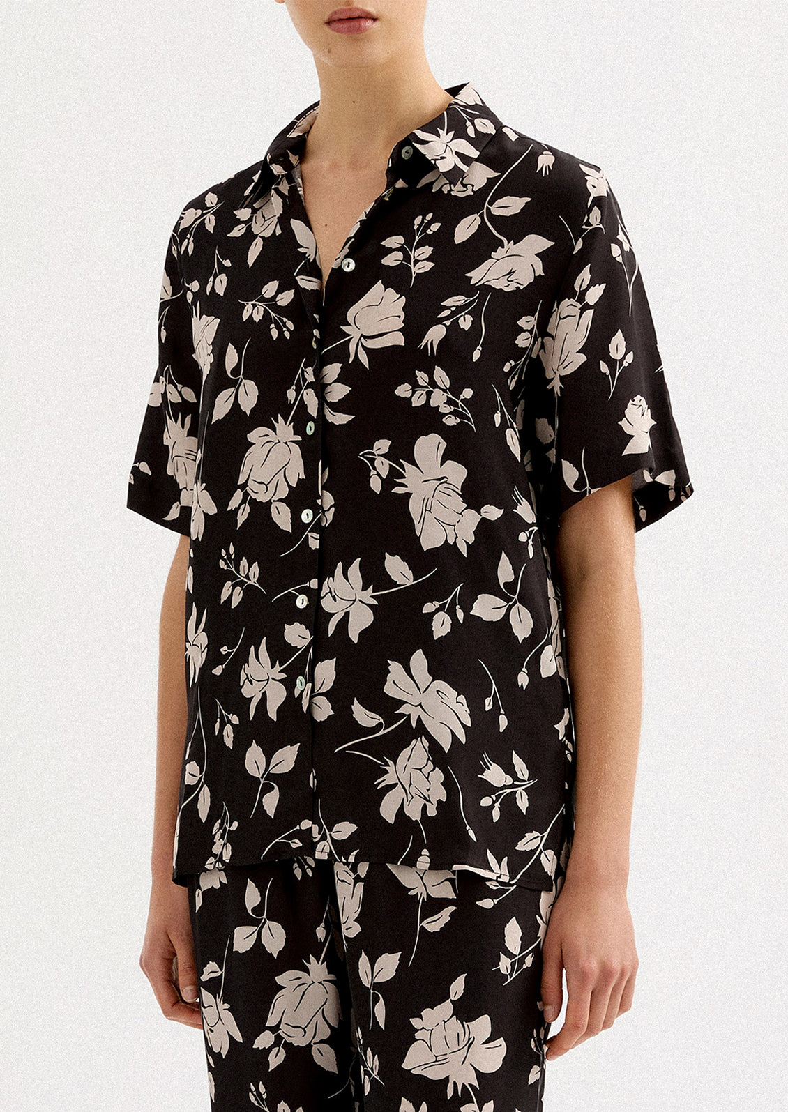 A person wearing a short sleeve collared shirt in black with white floral pattern.