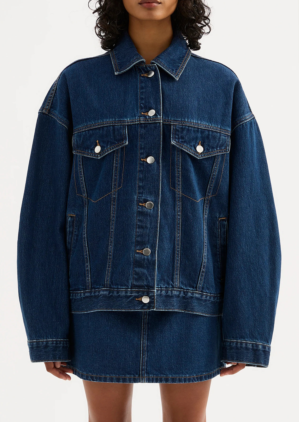 A woman wearing an oversized denim jacket in dark wash.