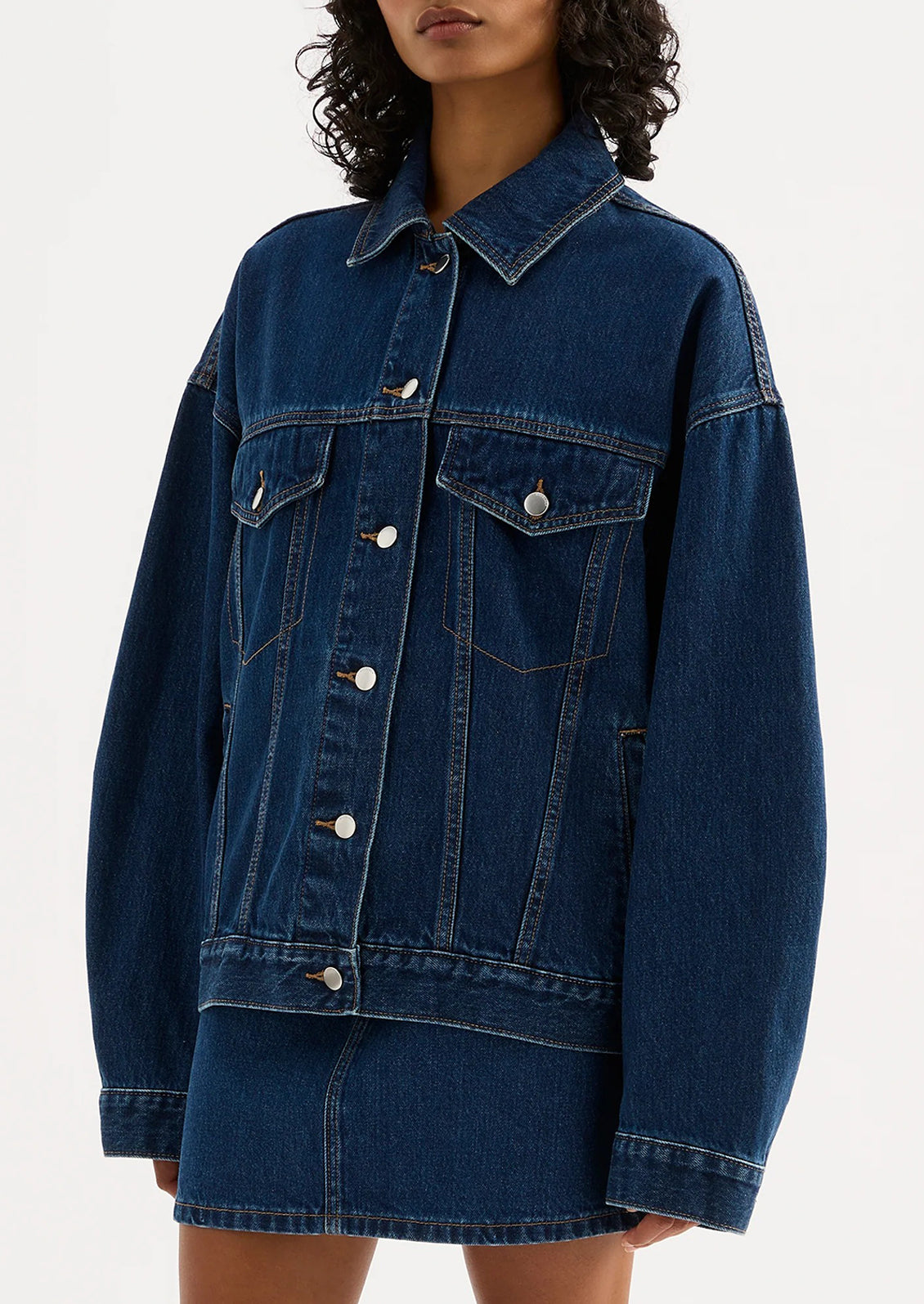 A woman wearing an oversized denim jacket in dark wash.