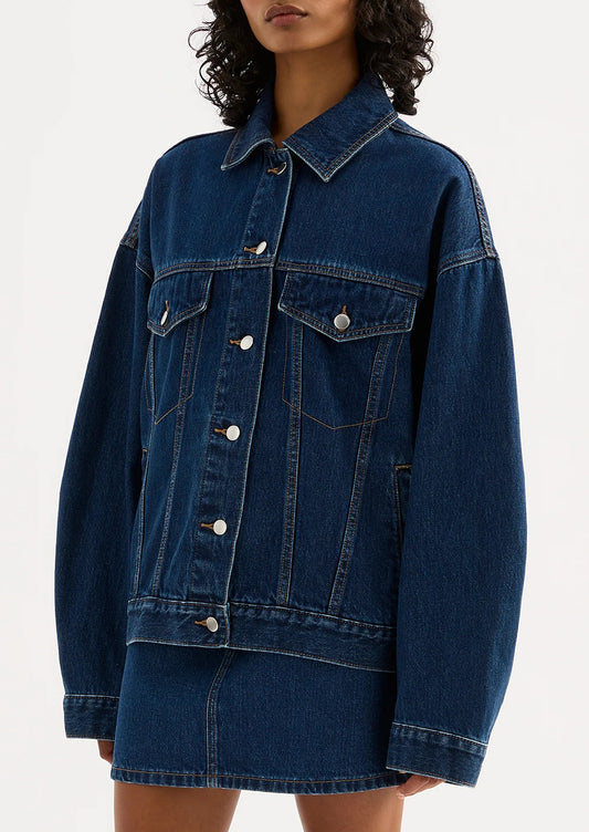 A woman wearing an oversized denim jacket in dark wash.