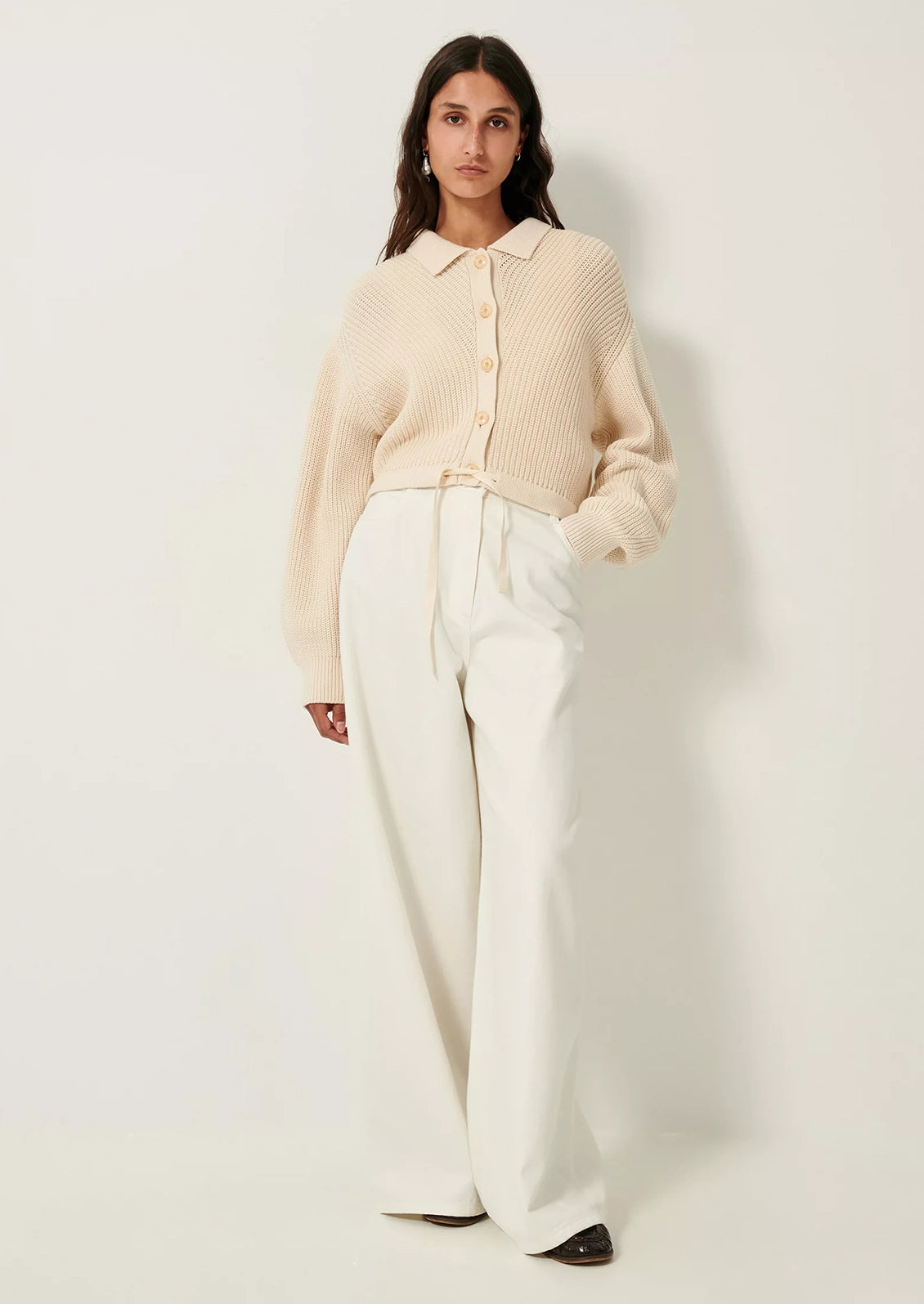 A woman wearing a cream knit sweater with collar, button front and tie waist.