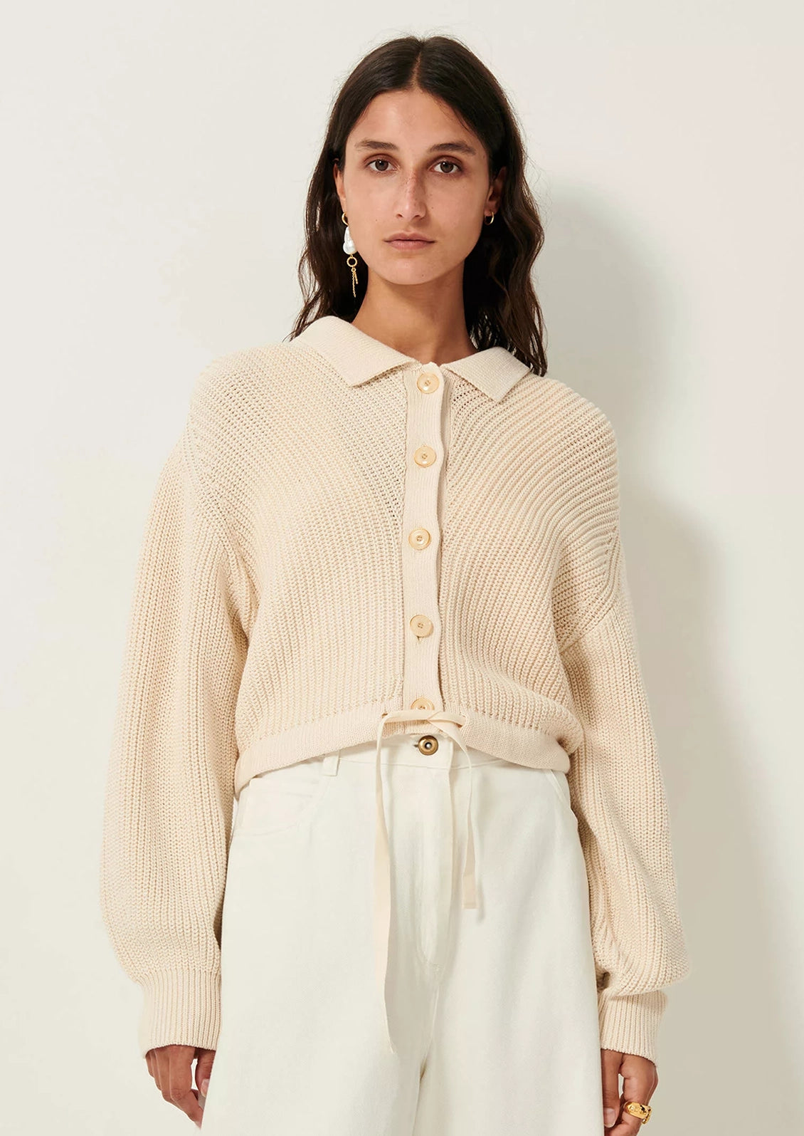 A woman wearing a cream knit sweater with collar, button front and tie waist.