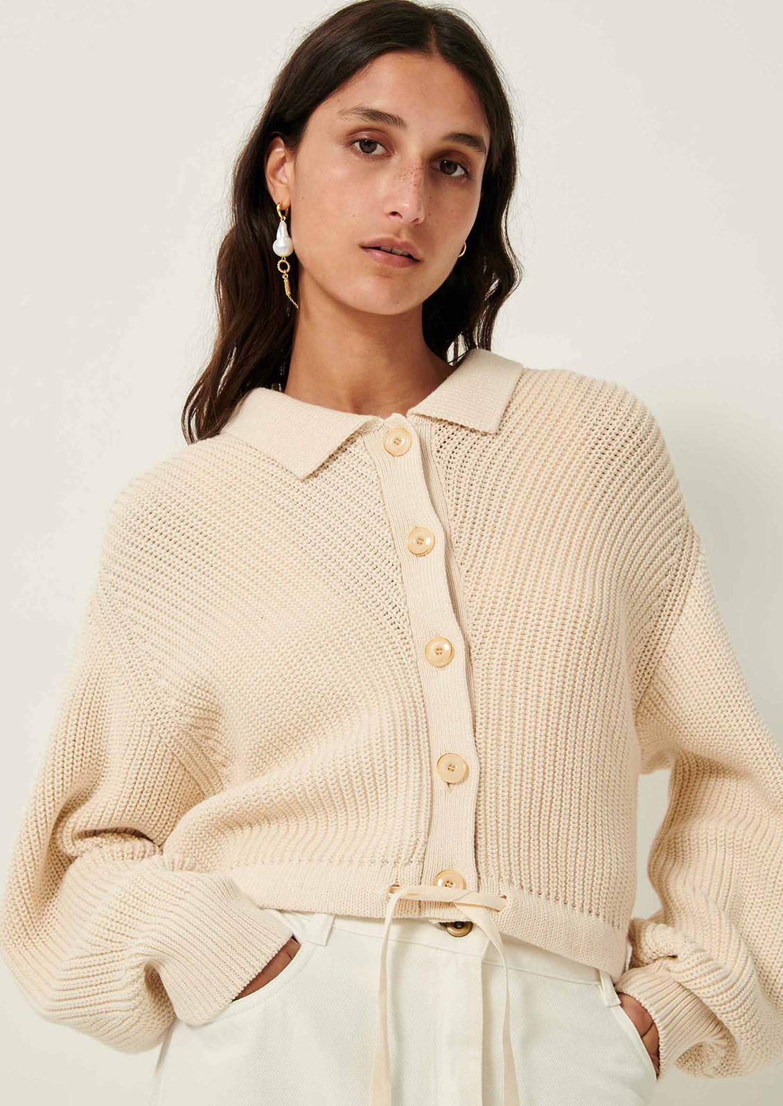A woman wearing a cream knit sweater with collar, button front and tie waist.