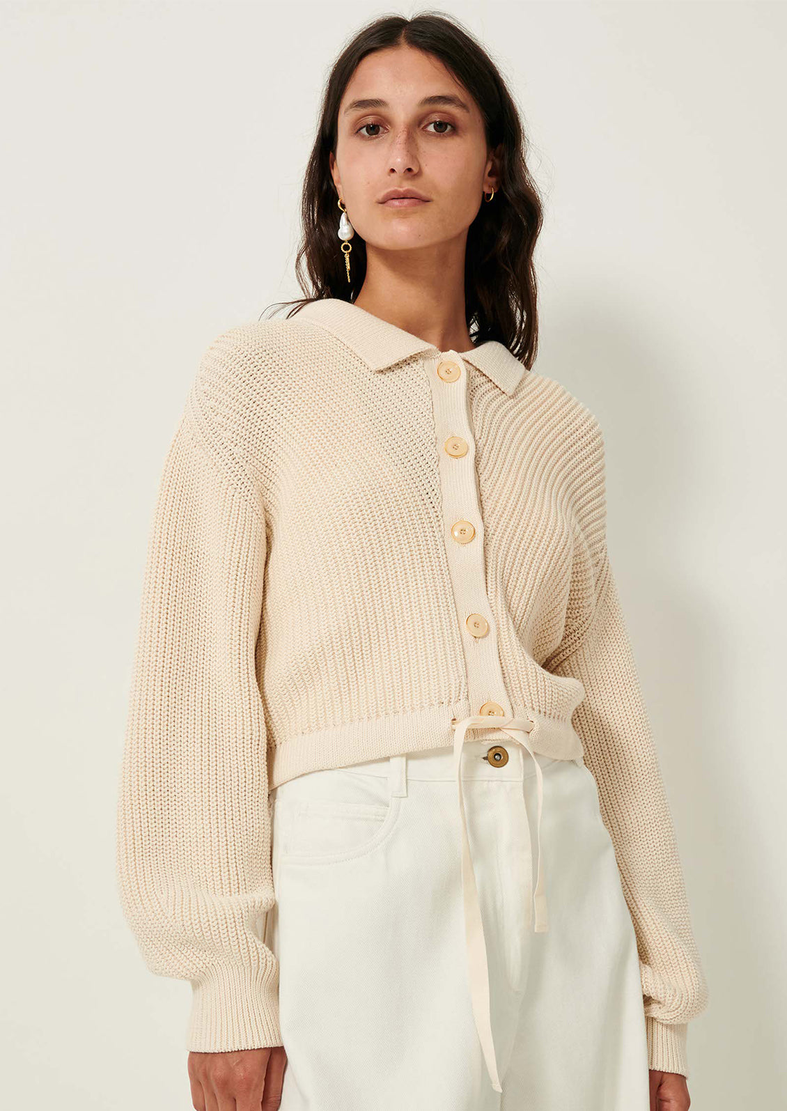 A woman wearing a cream knit sweater with collar, button front and tie waist.